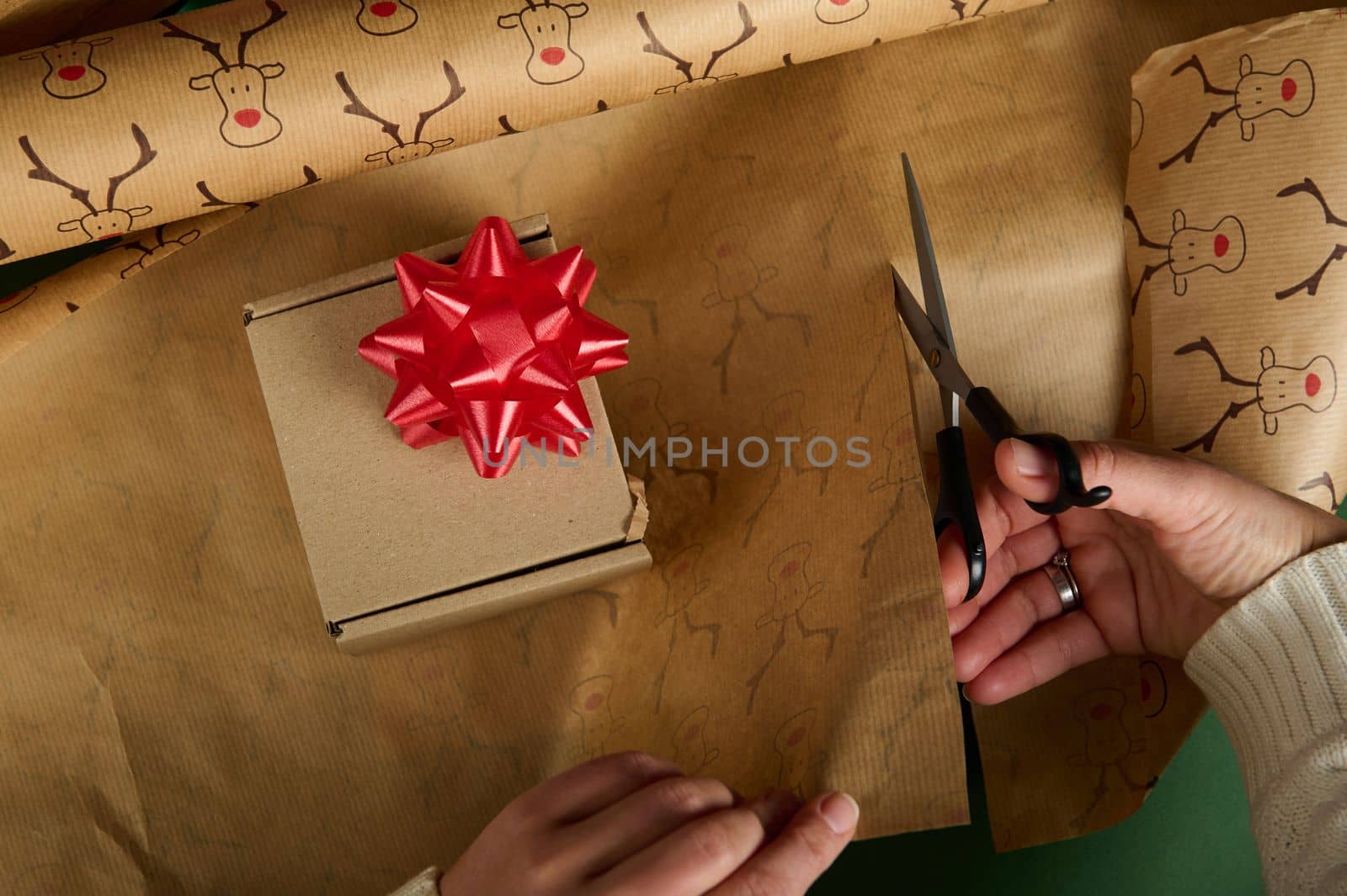Top view: Wrapping Christmas present in decorative paper with deer pattern and red bow. Boxing Day. Diy gift. Copy space by artgf