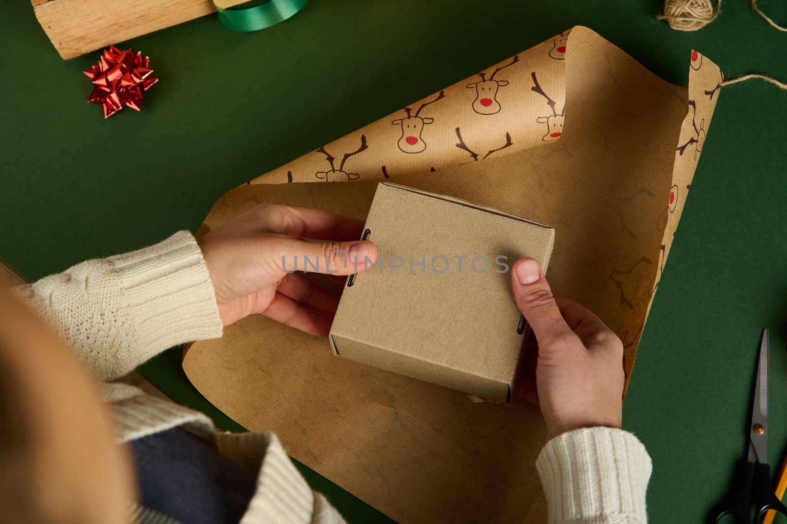 Top view of unknown woman holding a cardboard box above a wrapping paper with deer pattern. Packing presents. Boxing Day. Magical atmosphere of winter holidays. Christmas and New Year's preparations