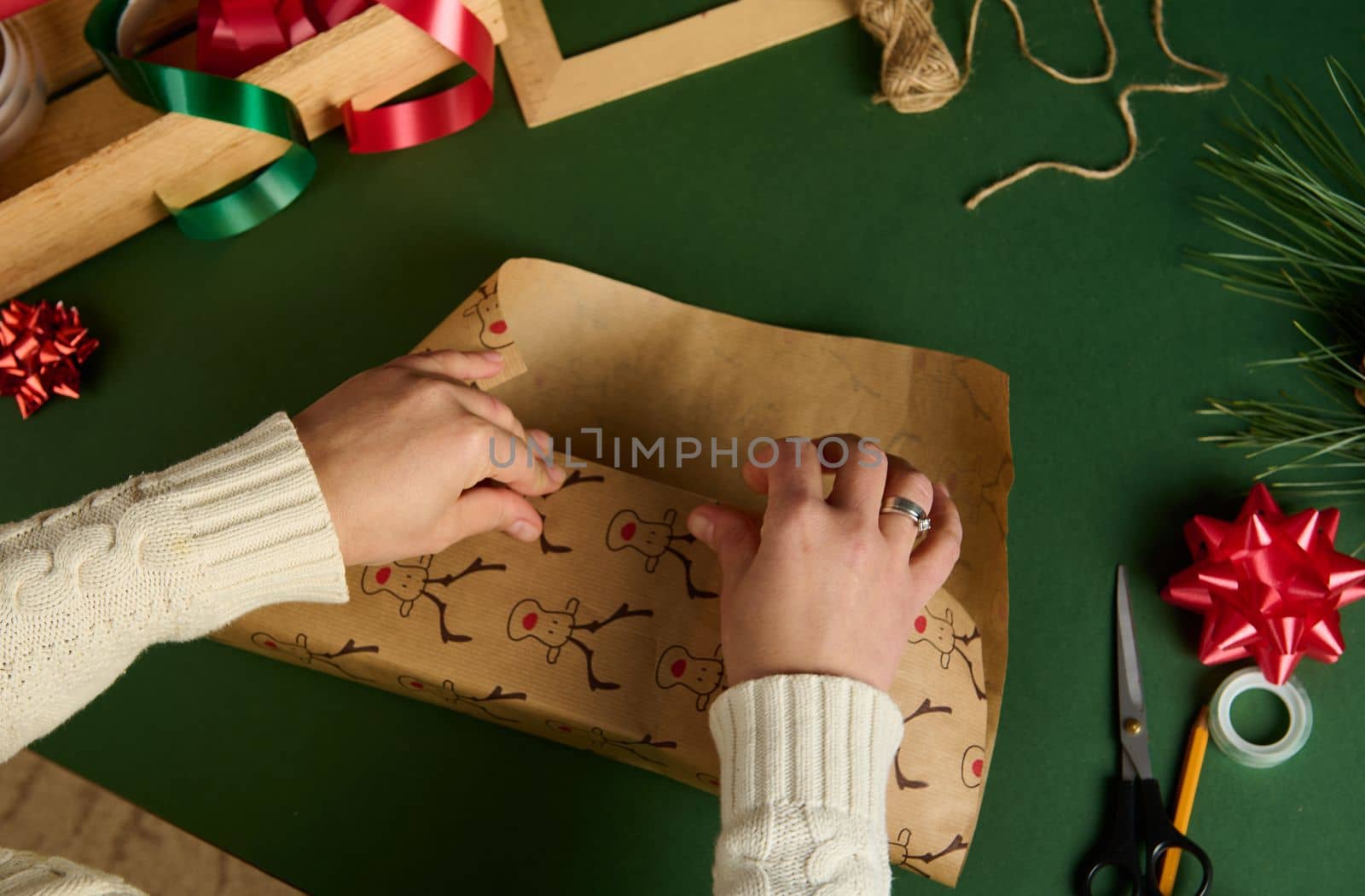 Top view of woman's hands wrapping a present for Christmas or New Year's events over green background. Boxing Day by artgf