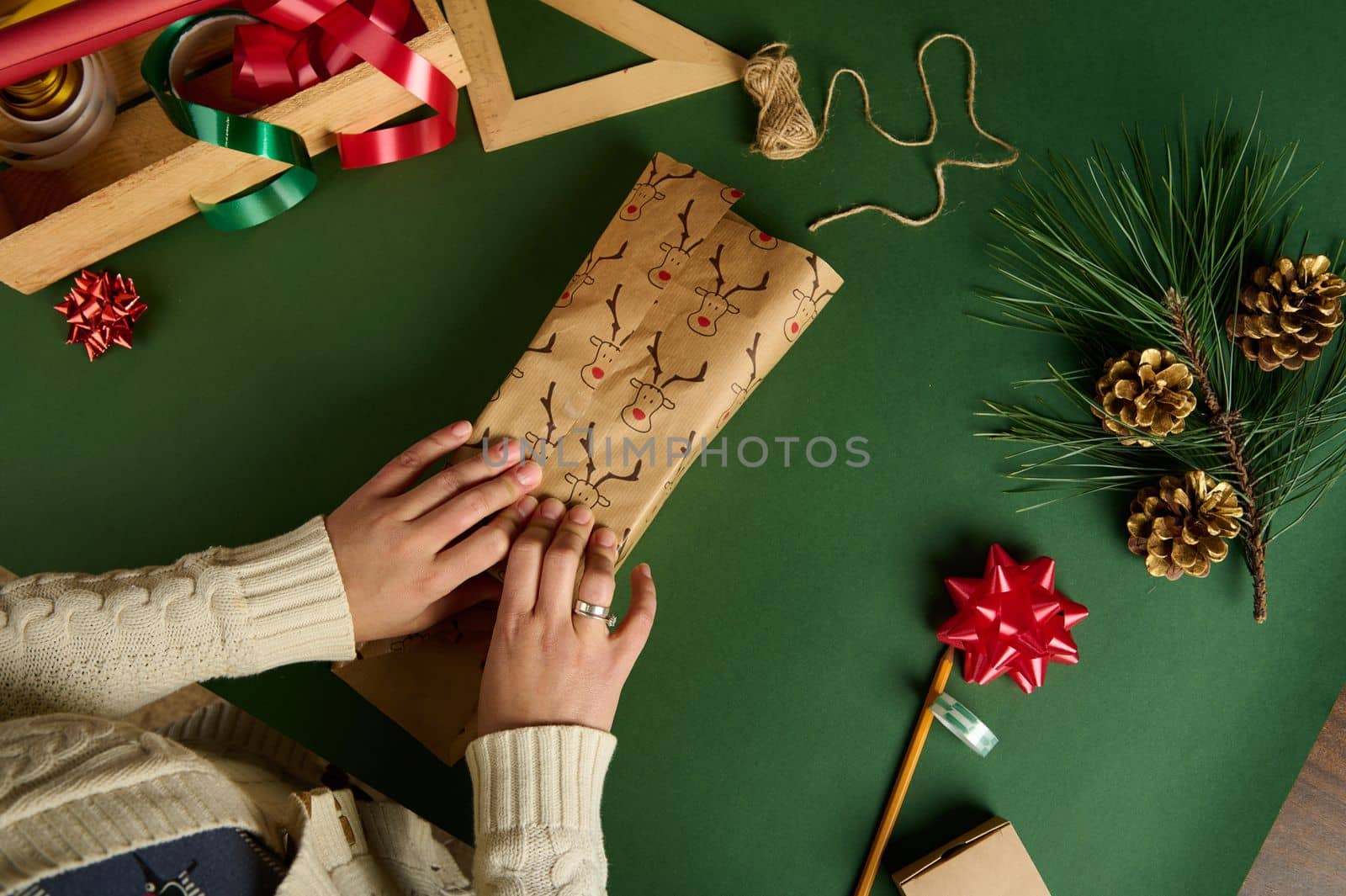 Top view of a woman packing present in decorative paper with deer pattern, over green background with wrapping materials by artgf