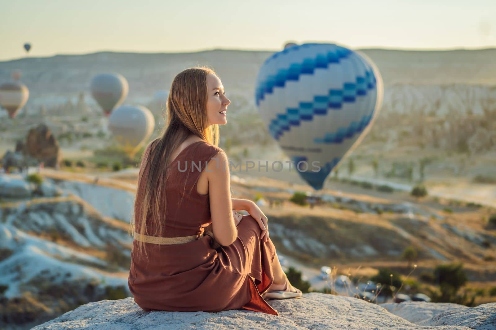 Tourist woman looking at hot air balloons in Cappadocia, Turkey. Happy Travel in Turkey concept. Woman on a mountain top enjoying wonderful view.