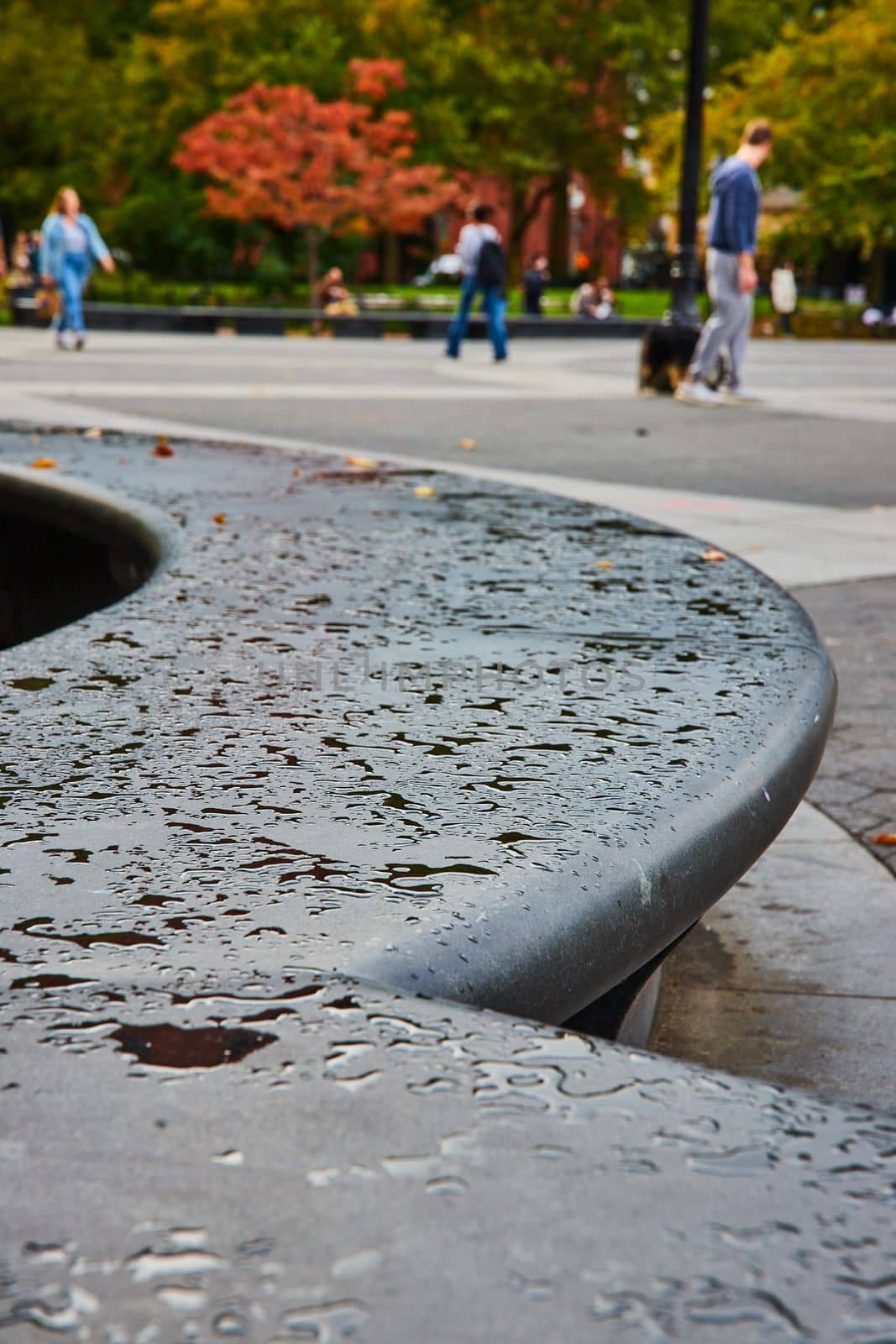 Image of Cement concrete curved seating with patches of water drops and tourists soft in background