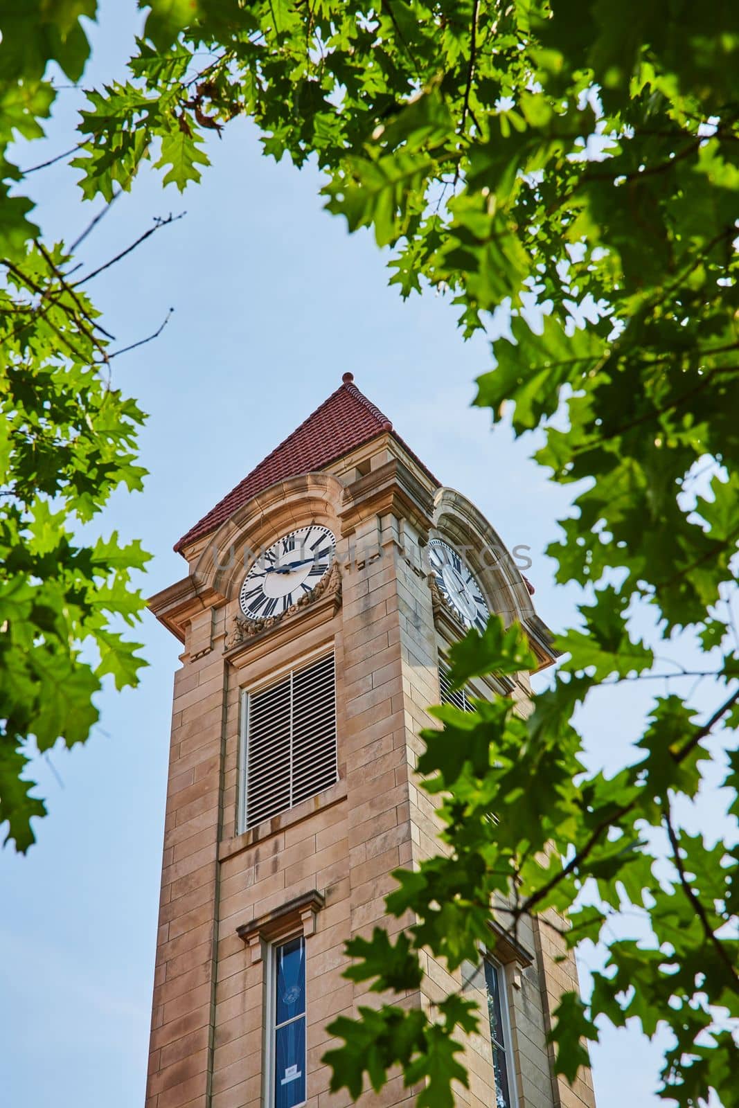 Green leaves frame limestone clock tower on college campus by njproductions