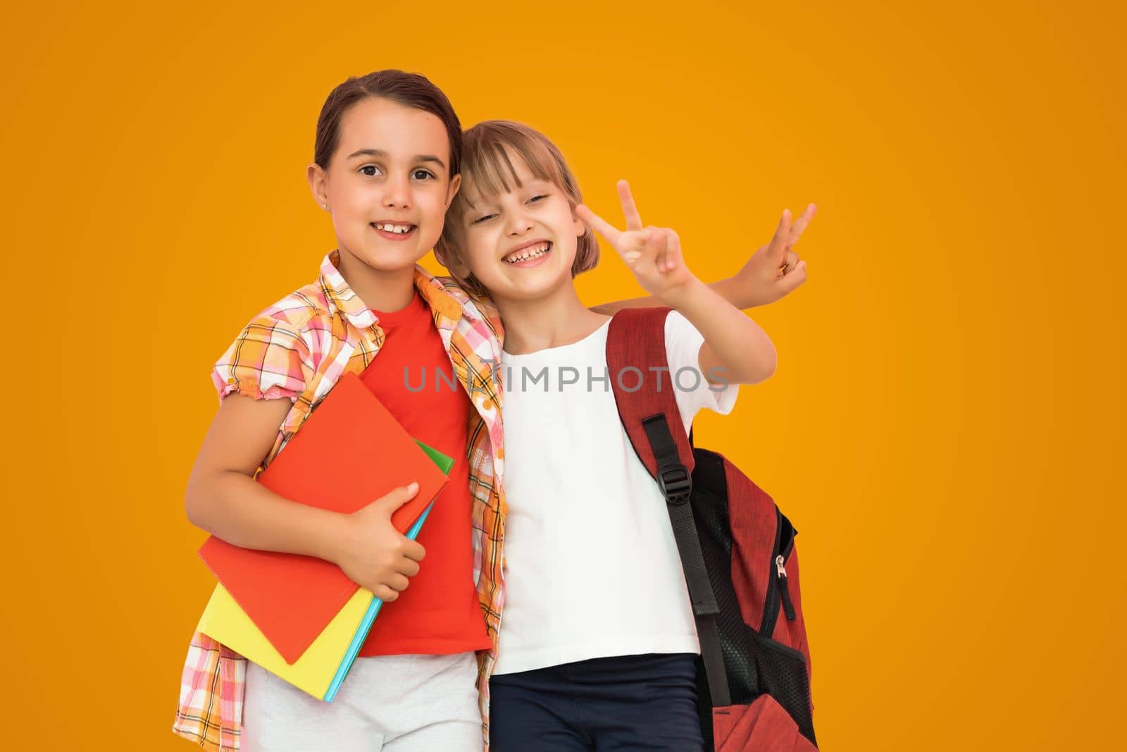 Photo of two small girls schoolchildren sister classmates hold books isolated orange color background.