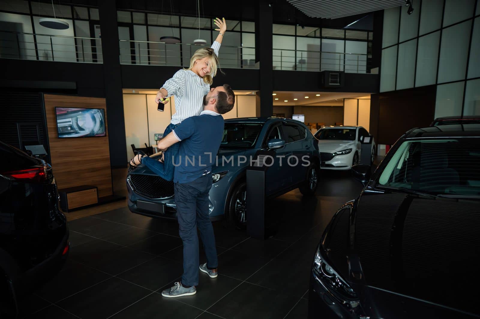 Happy caucasian couple hugging while buying a new car in a car dealership