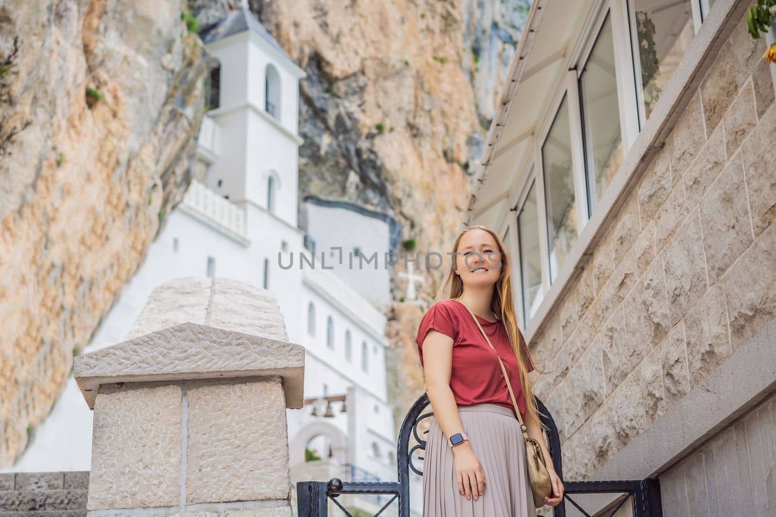 Woman tourist in Monastery of Ostrog, Serbian Orthodox Church situated against a vertical background, high up in the large rock of Ostroska Greda, Montenegro. Dedicated to Saint Basil of Ostrog.