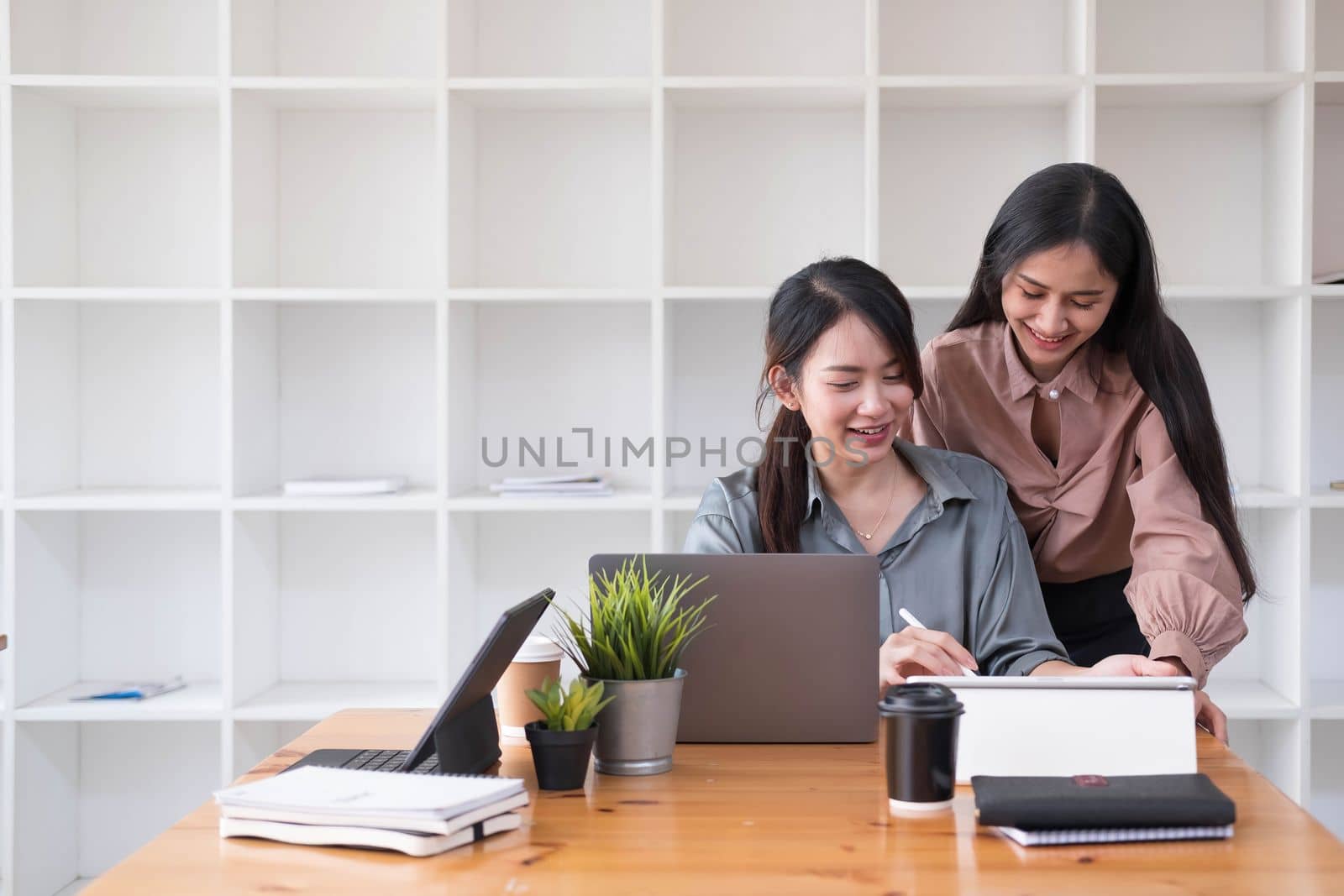 Two young Asian business woman talk, consult, discuss working with new startup project idea presentation analyze plan marketing and investment in the office. by wichayada