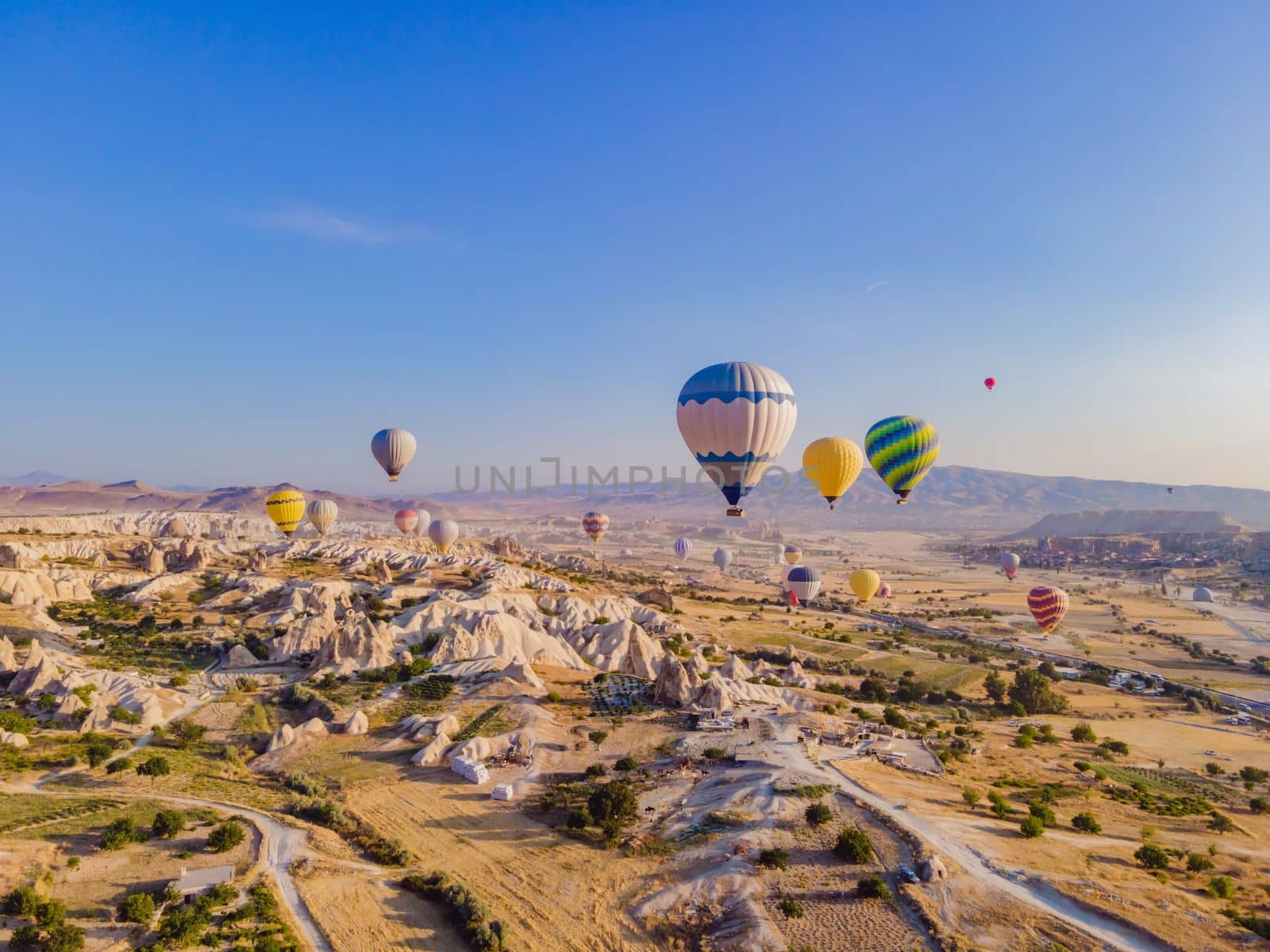 Colorful hot air balloons flying over at fairy chimneys valley in Nevsehir, Goreme, Cappadocia Turkey. Spectacular panoramic drone view of the underground city and ballooning tourism. High quality.