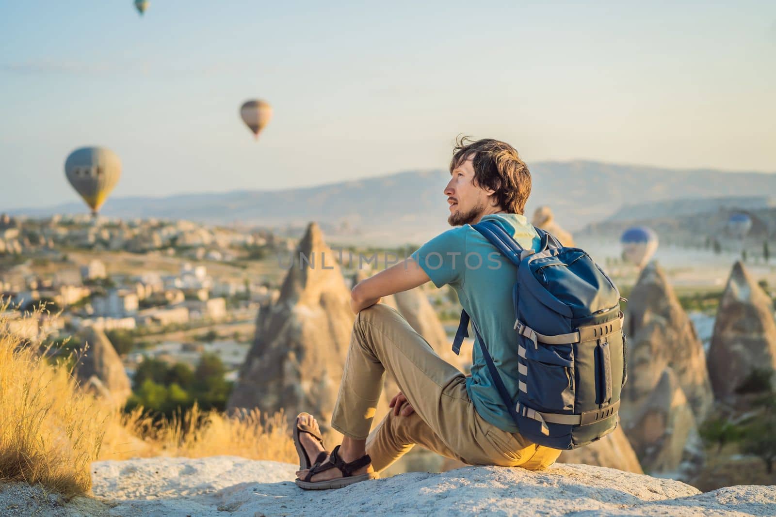 Tourist man looking at hot air balloons in Cappadocia, Turkey. Happy Travel in Turkey concept. Man on a mountain top enjoying wonderful view.