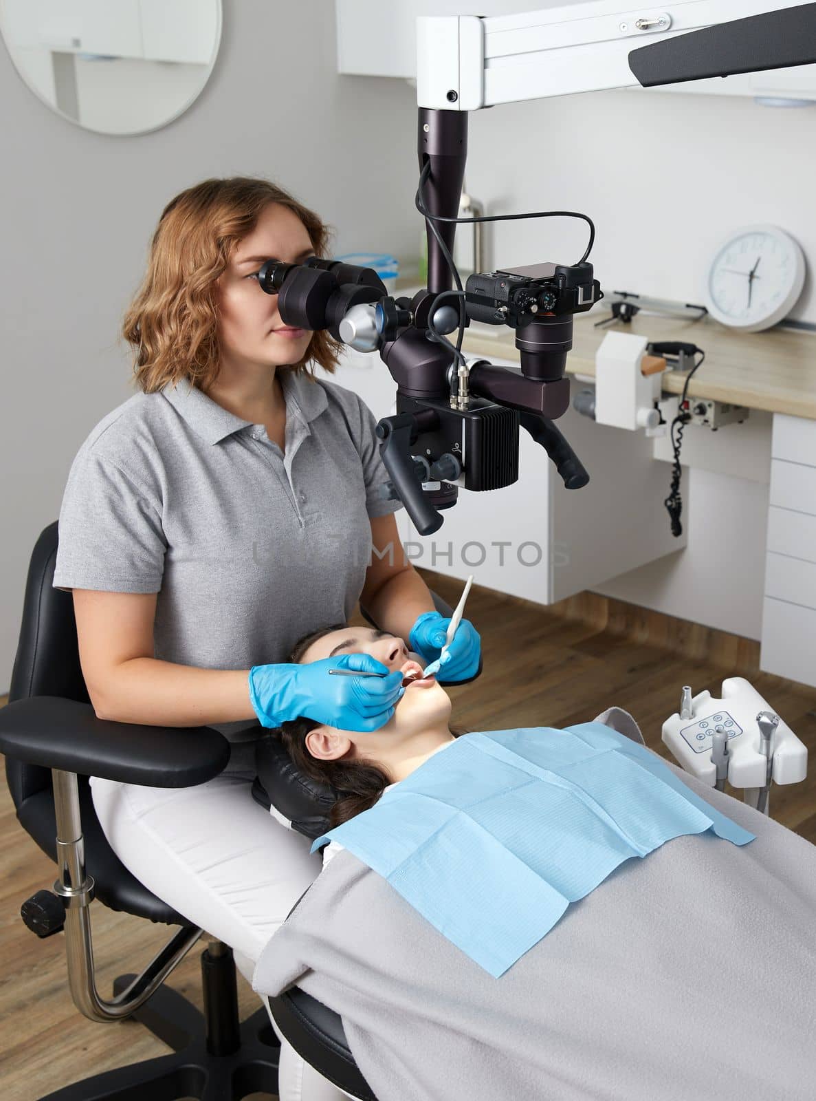 Female dentist with microscope treating patient teeth at dental clinic office. Medicine, dentistry and health care concept. by Mariakray