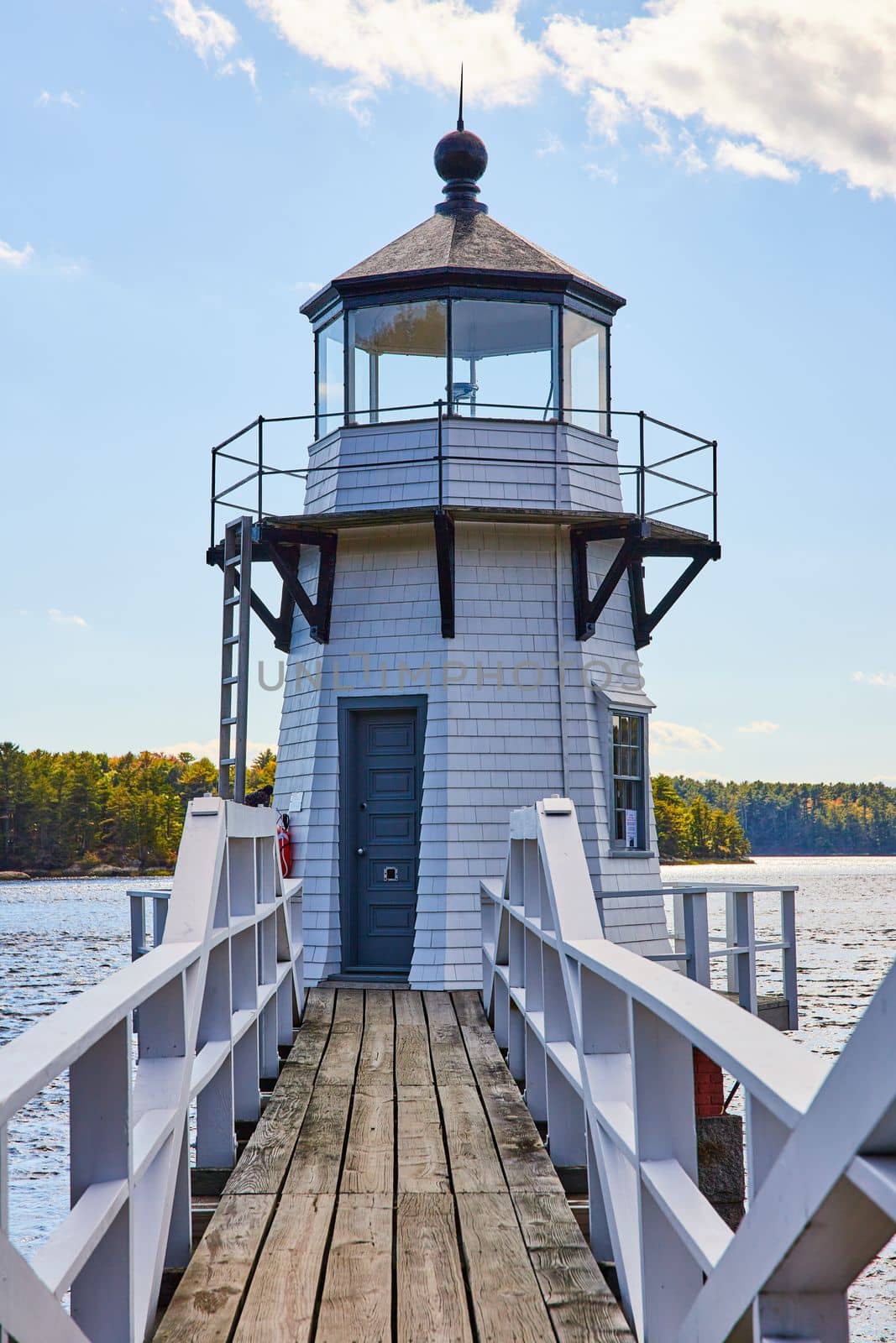 Image of Boardwalk with railing leads to small white lighthouse on Maine river