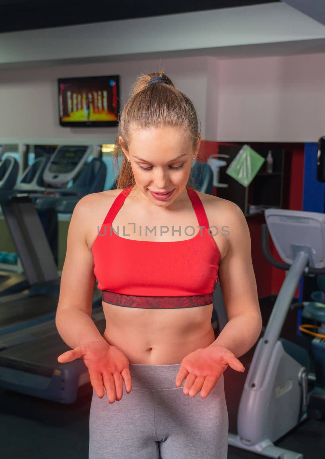 Young woman in sportswear having ache on palms after training in a gym