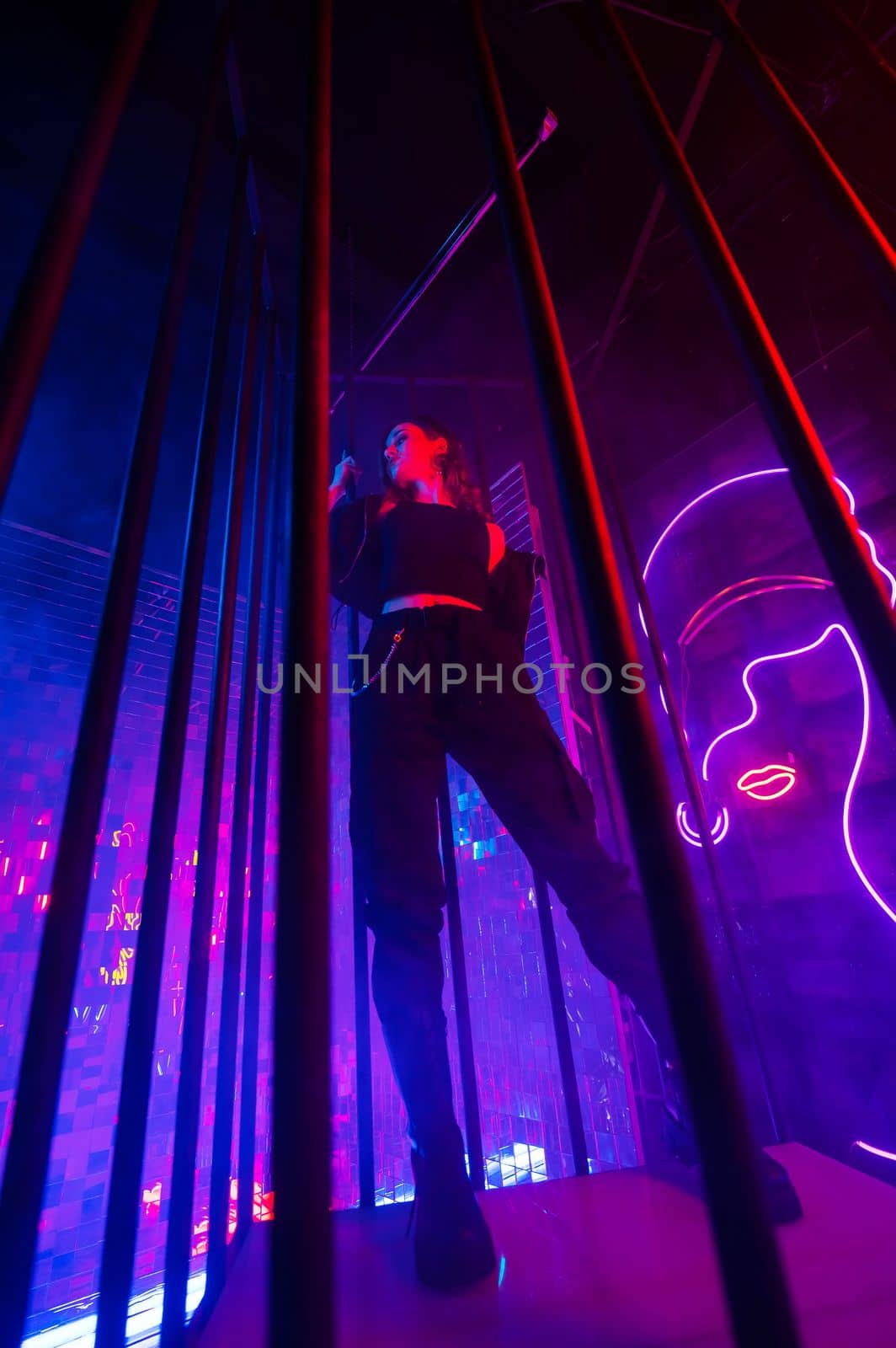 Caucasian woman in neon studio behind steel bars