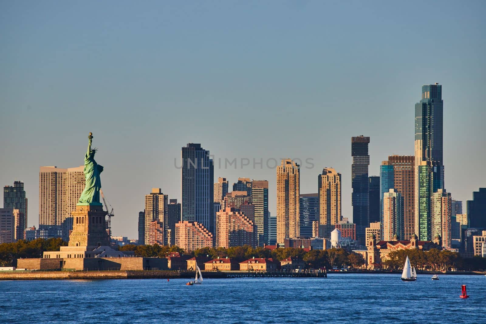 Statue of Liberty with skyscrapers surrounding from waters in golden light by njproductions