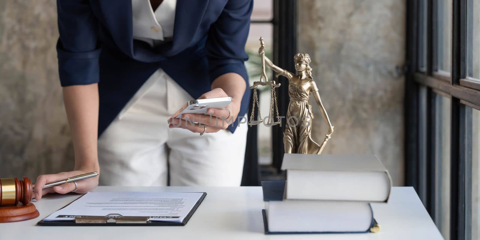 Attractive young lawyer or Businesswoman talking on phone and lawyers discussing contract papers with brass scale on wooden desk in office. Law, legal services, advice, Justice and real estate concept..