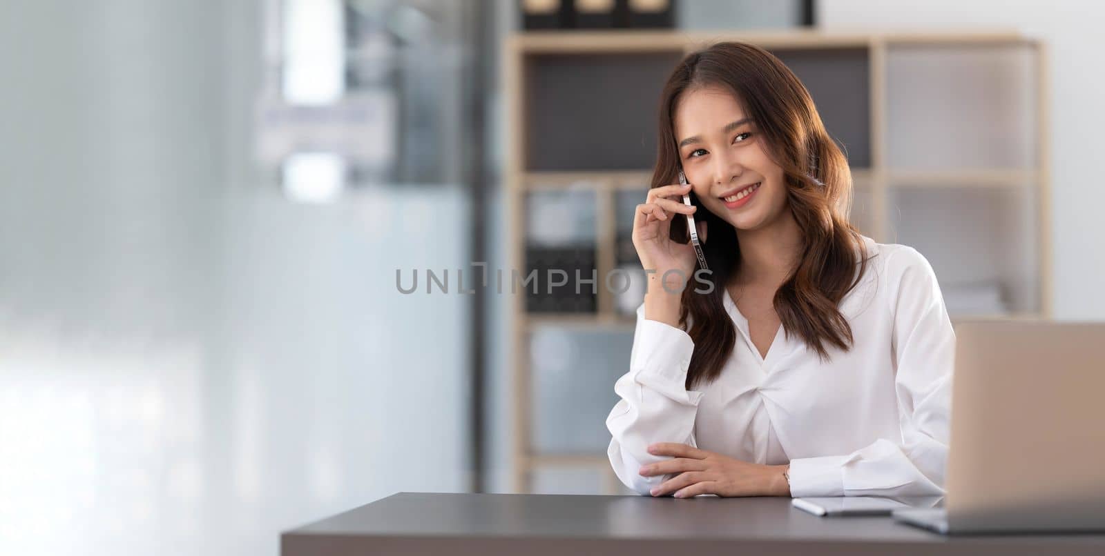Young Asian businesswoman sit with her laptop computer happily talking on the phone with her customer explaining the detail in the office...