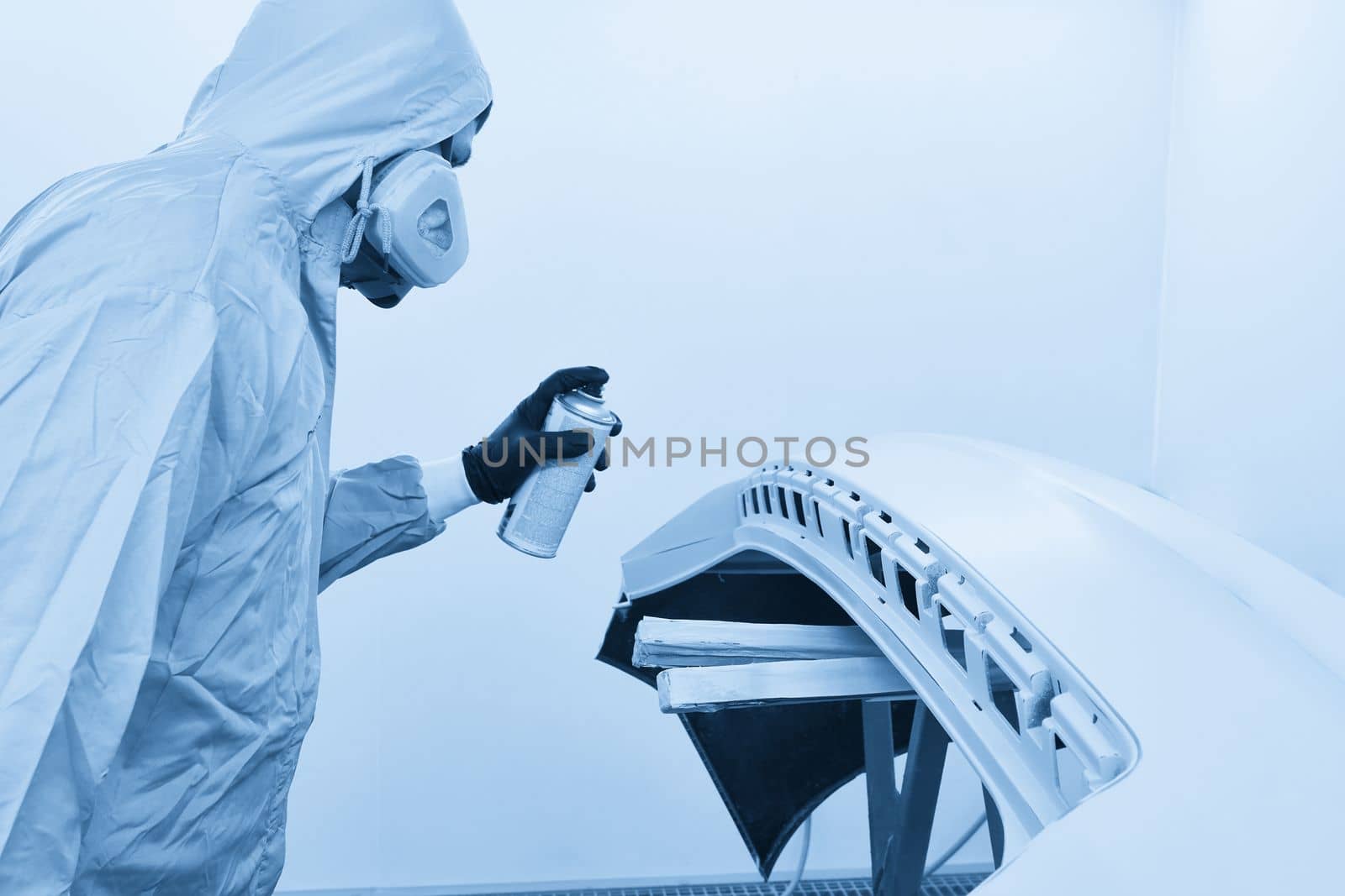 Mechanic painting bumper of a car with sprayer in painting booth