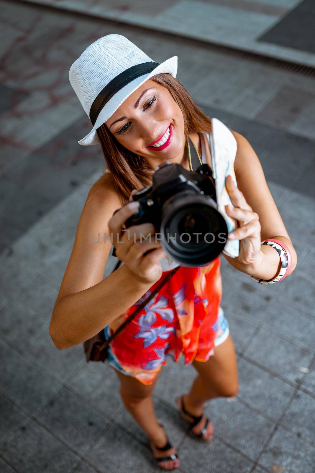 Beautiful young girl tourist holding map and photographing with digital camera.