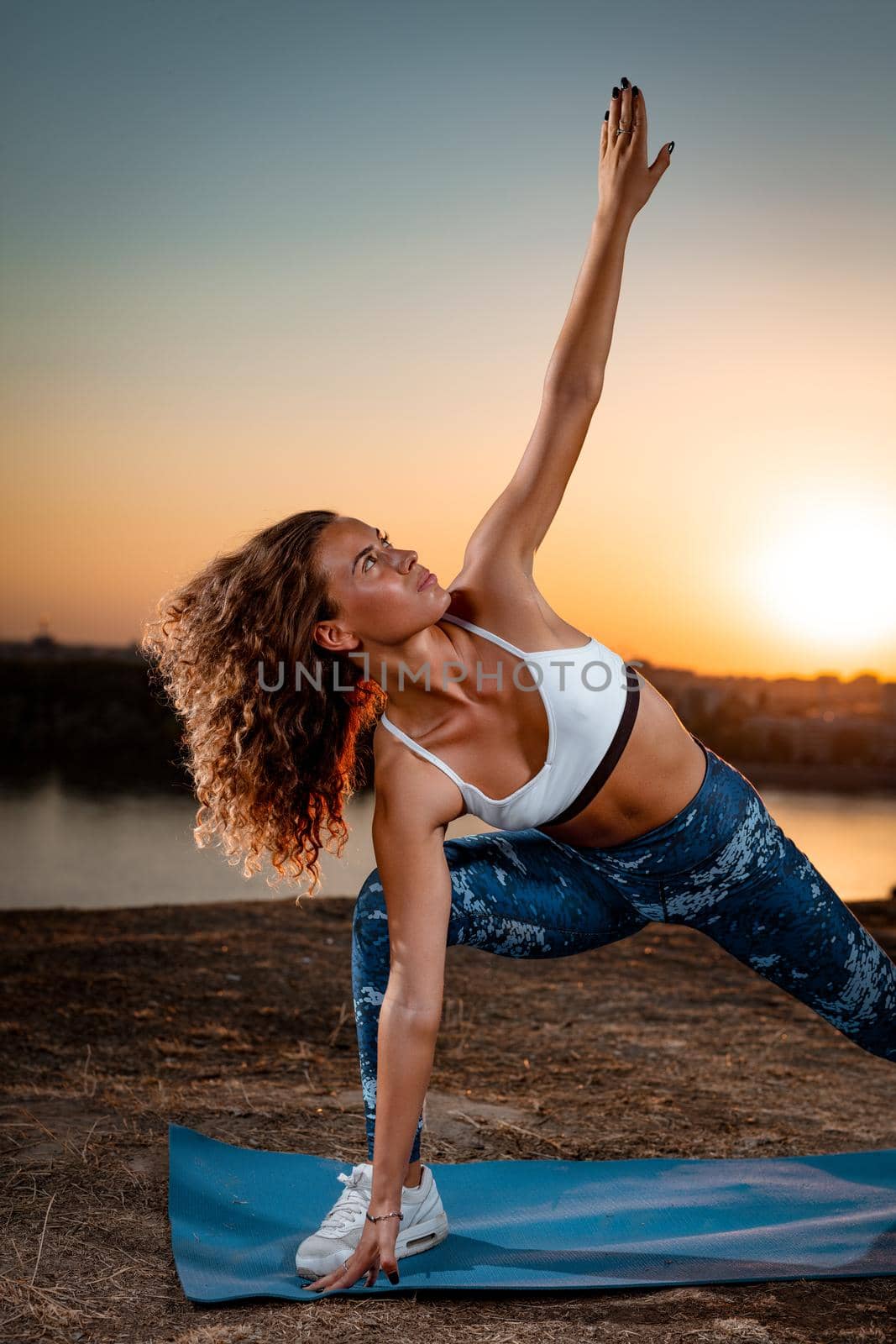 Young urban woman doing stretching exercises by the river in a sunset.