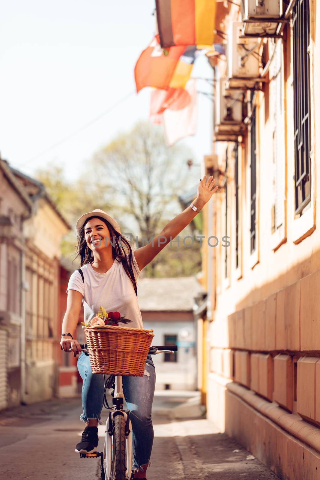 Happy woman riding the bike along the city street, in summer sunny day, smiling of joy during outdoor activity. 