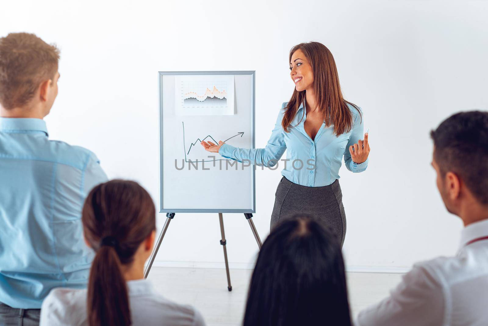 Businesspeople having meeting in a office. Young businesswoman standing in front of flip chart and having presentation.