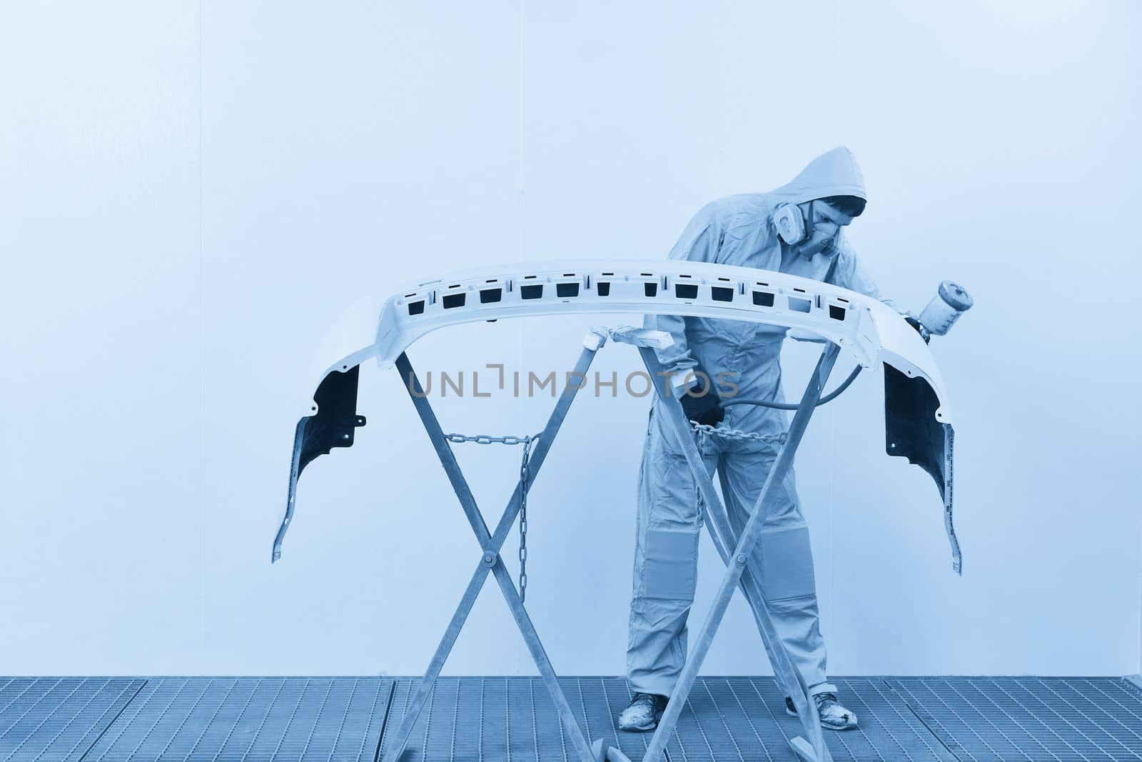 Mechanic painting bumper of a car with sprayer in painting booth