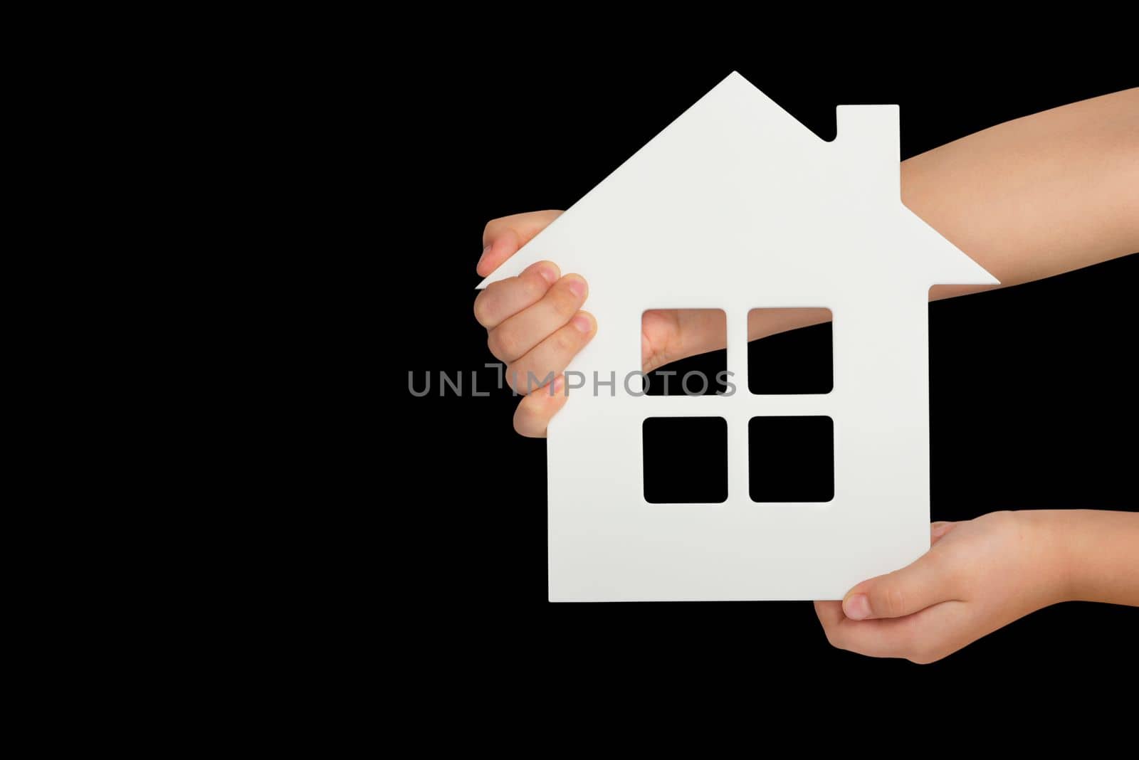 House in hand, isolation. White model of a house in the hands of a child isolated on a black background. Homeless housing, family home, home insurance, international family day.