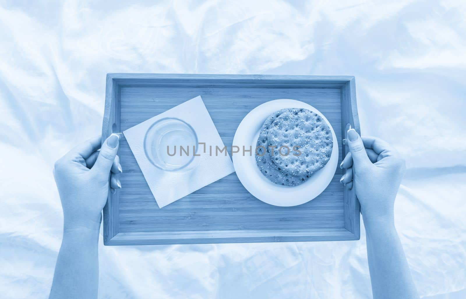 Woman holding tray with diet breakfast of crackers and water on bed