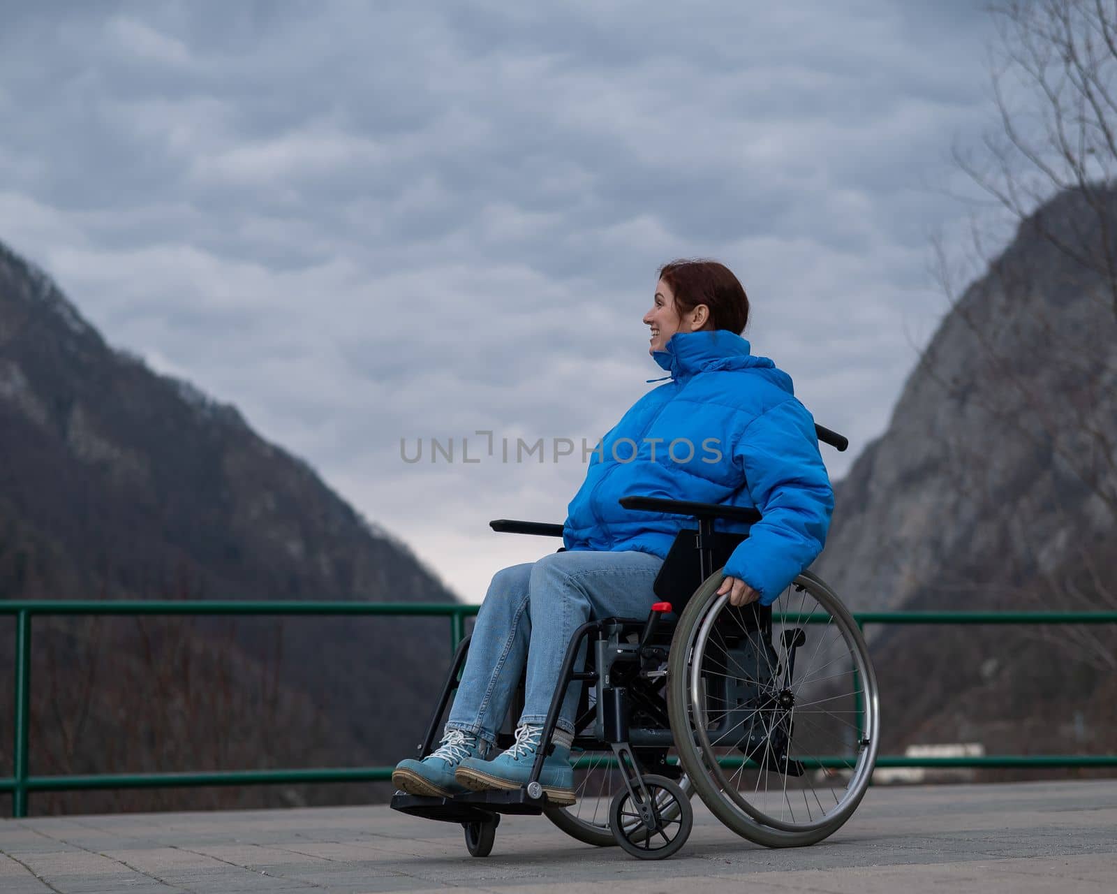 A woman in a wheelchair on a point view admires the high mountains. Thrust to life