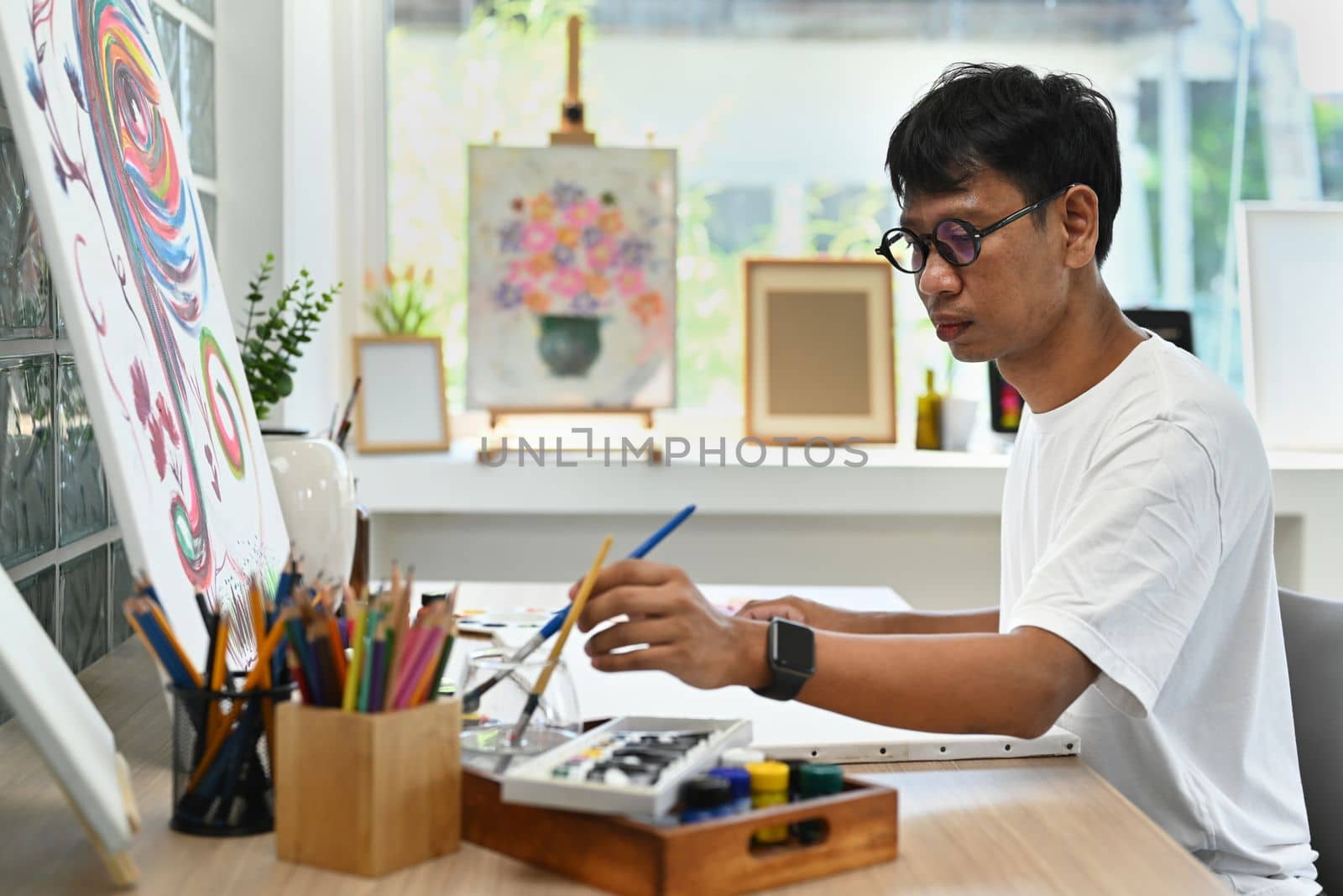 Asian man artist sitting in art studio and painting picture on canvas with oil paints. Art and leisure activity concept by prathanchorruangsak