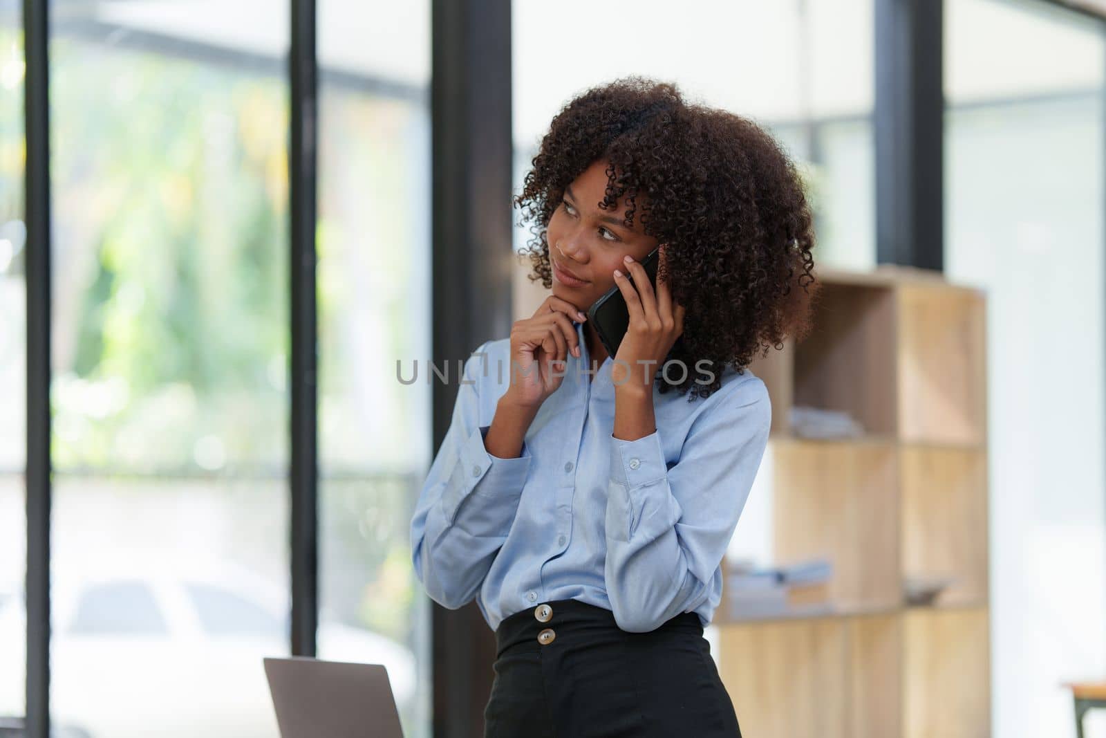 Business black woman having phone conversation with client in office. African american young woman using smart phone.