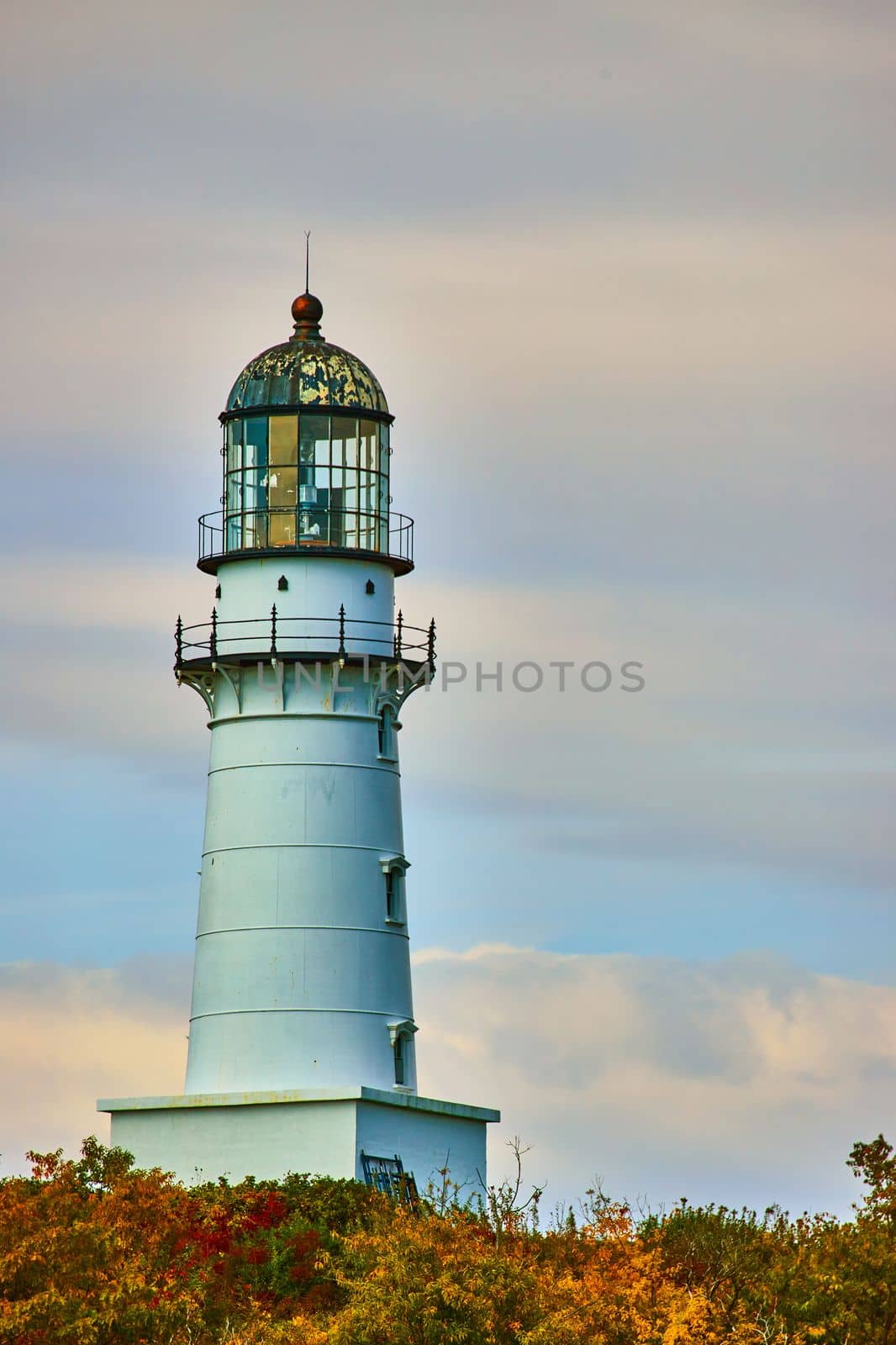 Image of Detail of large iconically shaped lighthouse in fall forest with cloudy sky