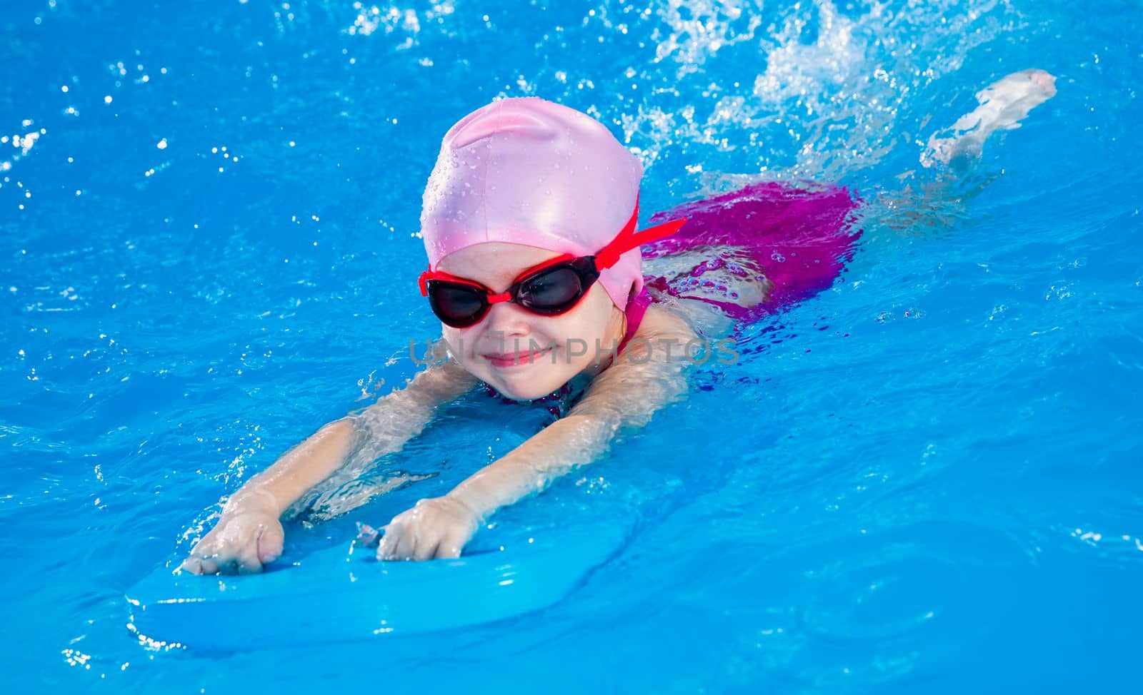 Preschool cute girl learning to swim in indoor pool with flutterboard