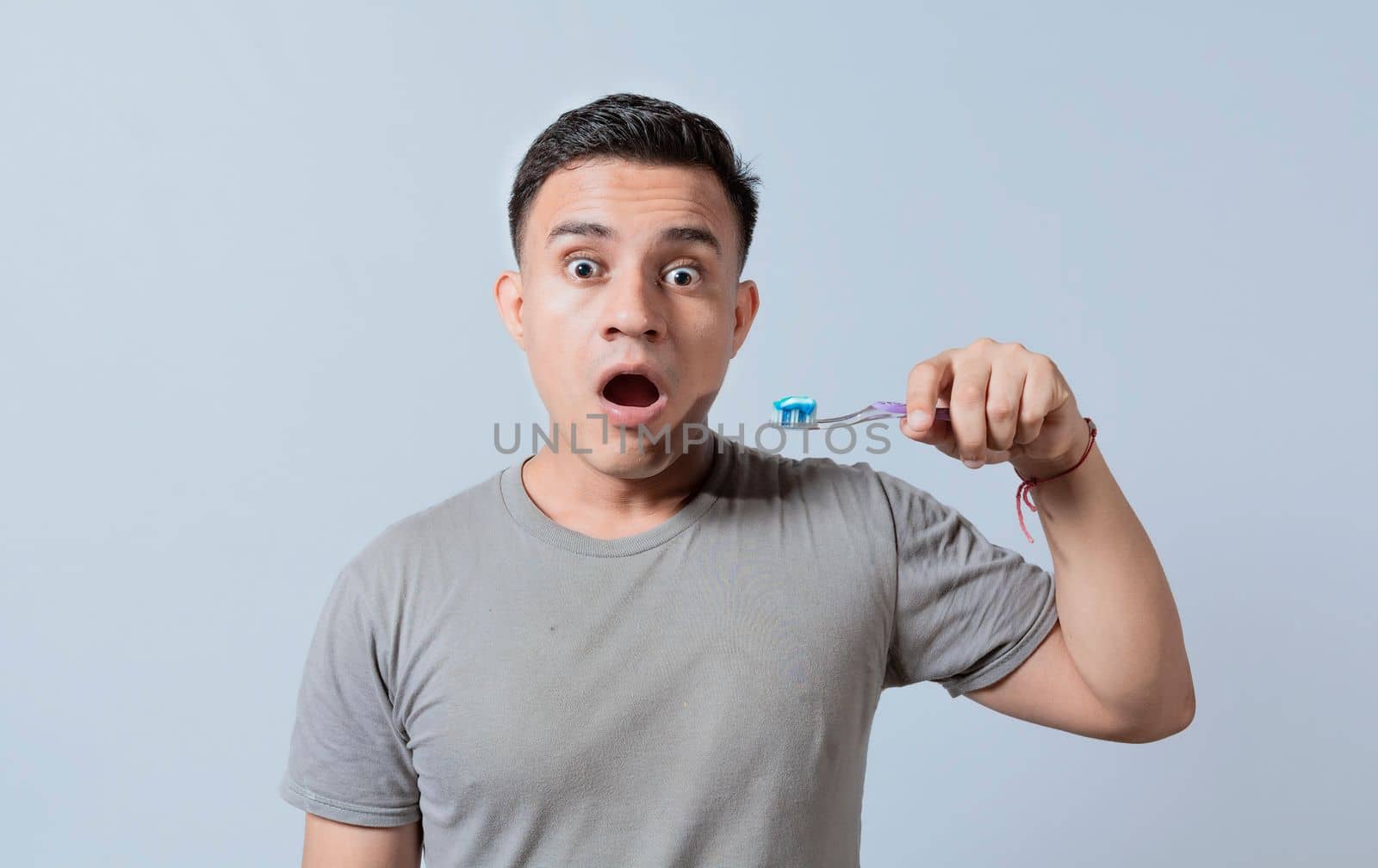 Amazed young man holding toothbrush with toothpaste isolated, guy with wow expression holding toothbrush isolated on white, Surprised young man holding a toothbrush with toothpaste
