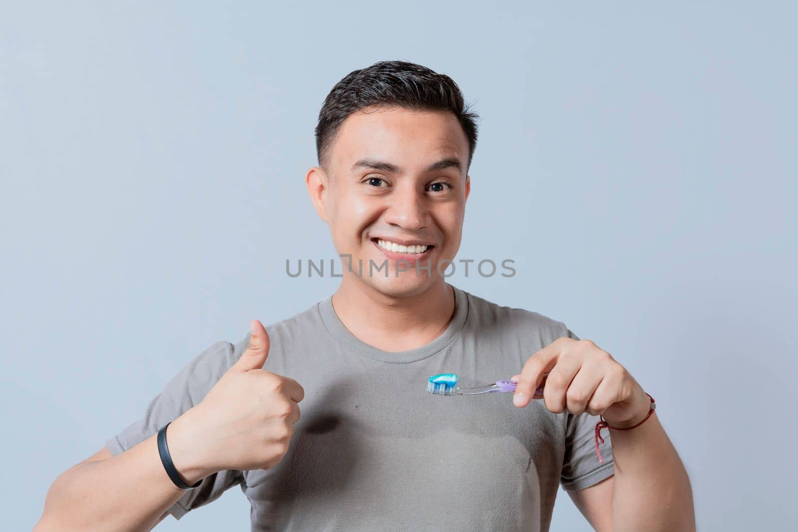 Smiling handsome guy holding a toothbrush with thumb up. Smiling people holding toothbrush with thumbs up gesture, Young man holding a toothbrush with thumb up isolated by isaiphoto