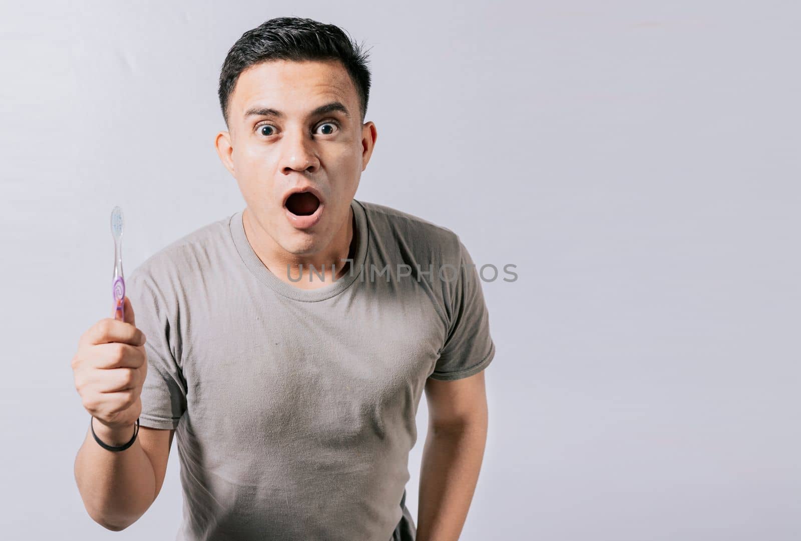 Guy holding toothbrush with amazed face isolated on white, Surprised young man holding a toothbrush. Amazed teenager holding toothbrush isolated
