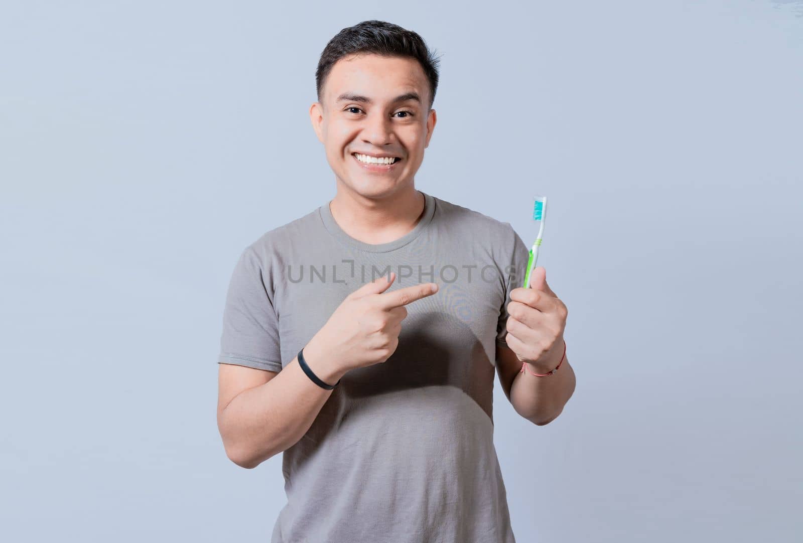 Handsome guy holding and pointing at toothbrush isolated. Person holding and pointing a toothbrush on isolated background, Smiling man holding and pointing at toothbrush by isaiphoto