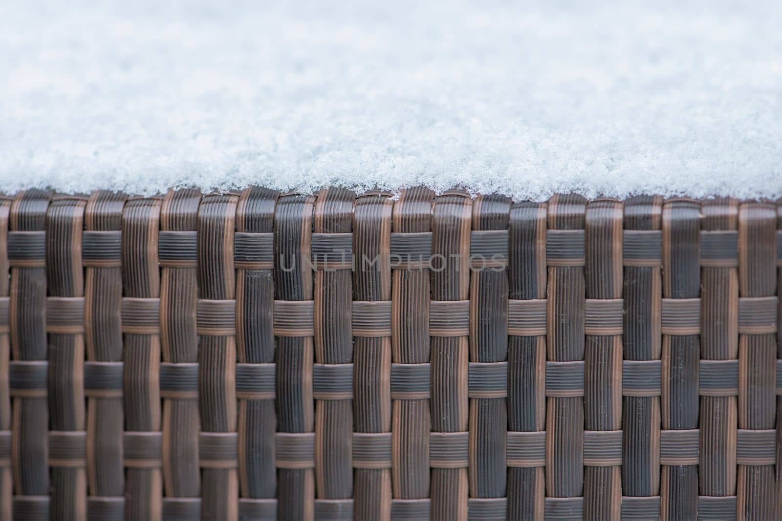 Care and storage of garden furniture in winter. texture of street furniture in winter. Artificial rattan covered with snow close-up. by SERSOL