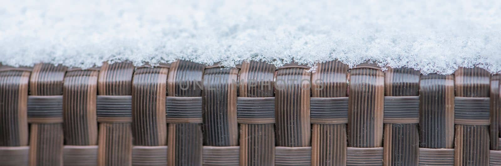 Care and storage of garden furniture in winter. texture of street furniture in winter. Artificial rattan covered with snow close-up