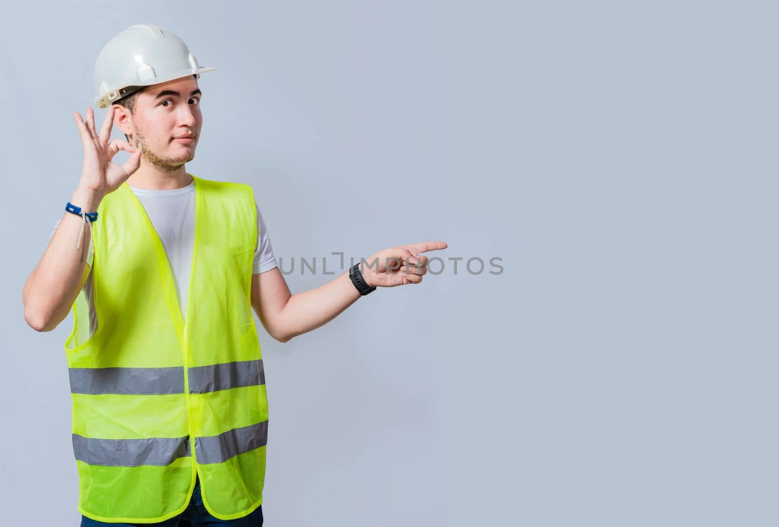 Handsome engineer recommending a product on white background, Young engineer pointing and recommending a product isolated. Builder engineer presenting a product with ok gesture