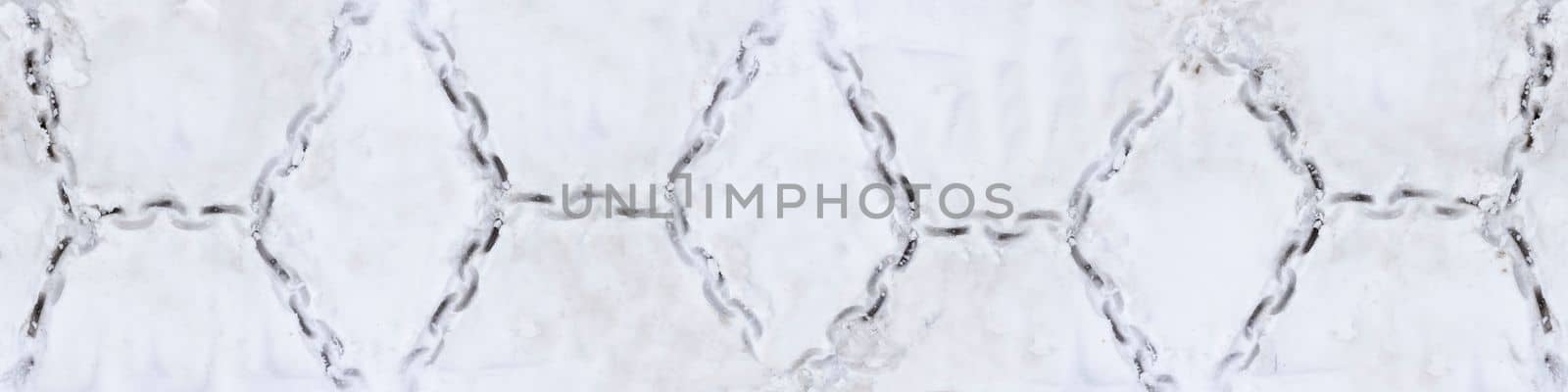 Tire texture on snow. Snow chain marks on an icy road. Track from the wheel of a car with a chain on the snow. by SERSOL