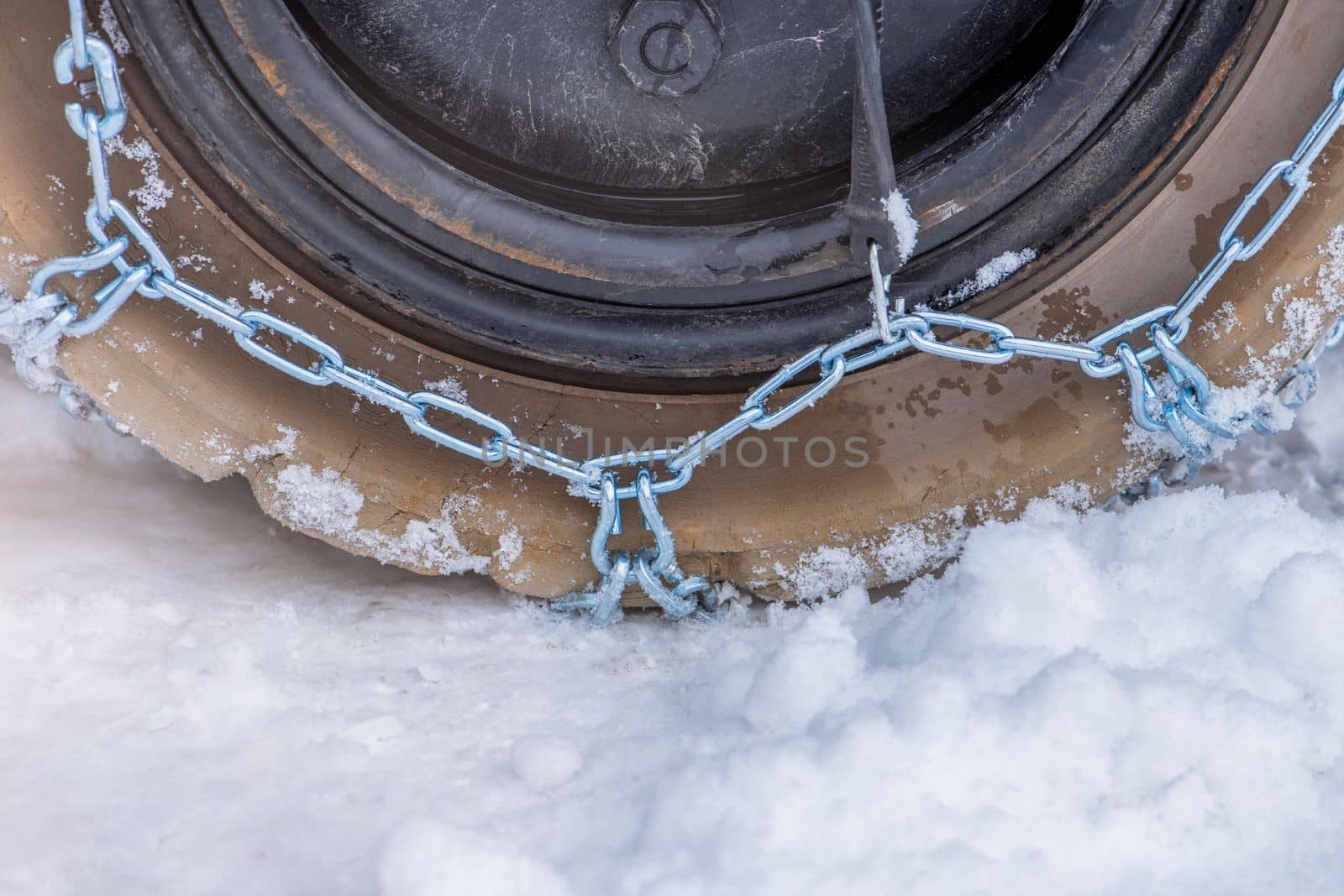 Wheel in the snow with safety and anti-skid chains. Loader or tractor with chains on wheels close-up. Driving safety in winter conditions.