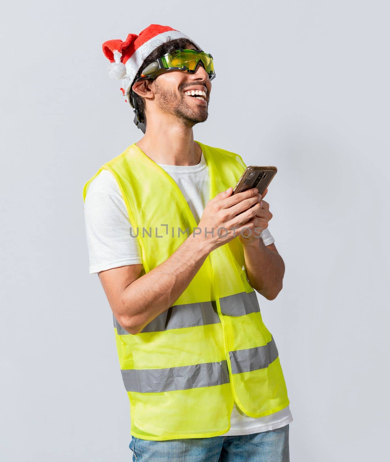 Happy Engineer in christmas hat using cell phone isolated. Smiling engineer in christmas hat using cell phone. Concept of engineer with christmas hat laughing while using cell phone at christmas