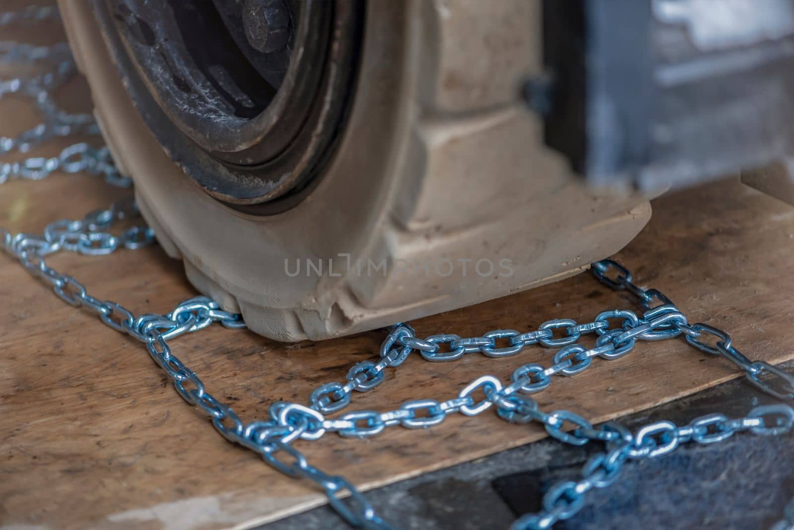The process of installing an anti-skid chain on a wheel in winter. Preparing a loader, tractor or truck for a snowy road. Snow chains close up.