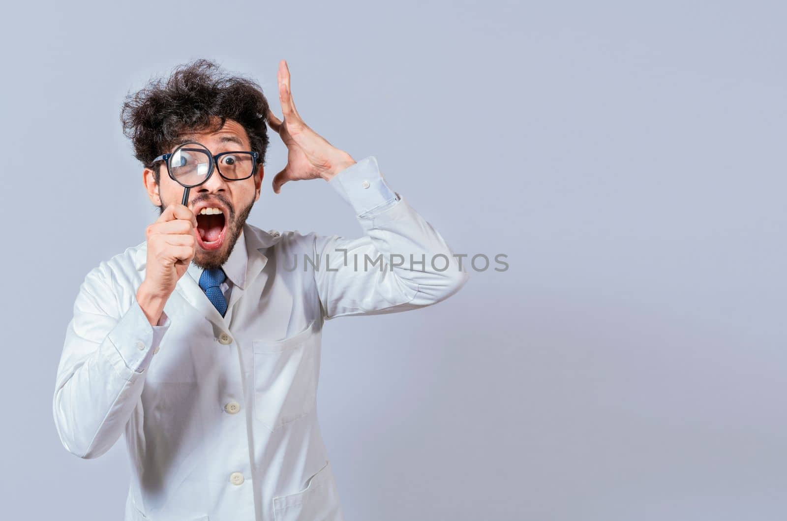 Surprised male scientist in lab coat looking at camera with magnifying glass. Mad scientist holding a magnifying glass isolated, Man in white coat with magnifying glass looking at camera