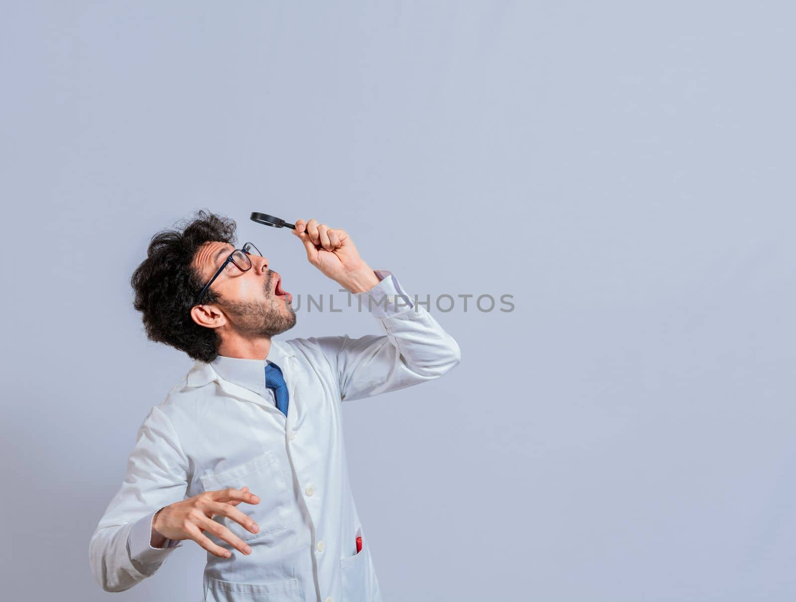 Surprised man in lab coat with magnifying glass looking at an advertisement above. Scientist man looking up with a magnifying glass. Amazed man observing an advertisement with a magnifying glass
