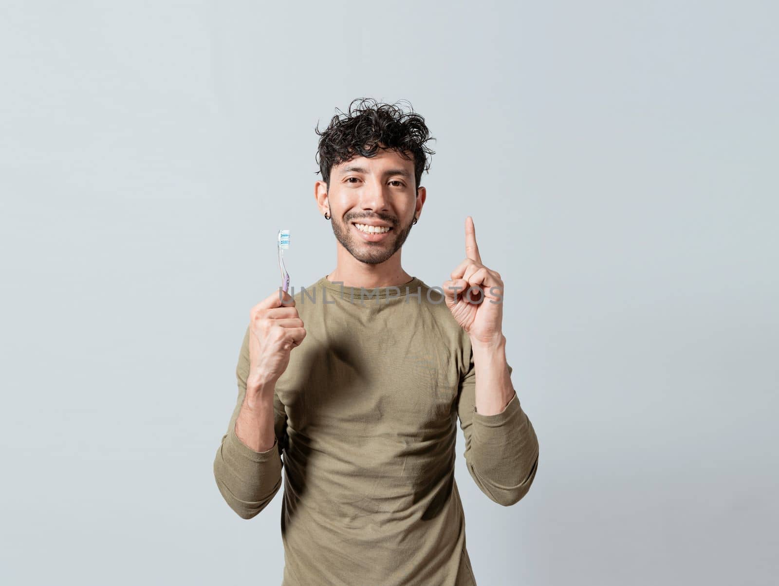 Smiling young man holding dental brush pointing up. Handsome guy holding toothbrush pointing an advertisement up. People holding toothbrush pointing to a blank space