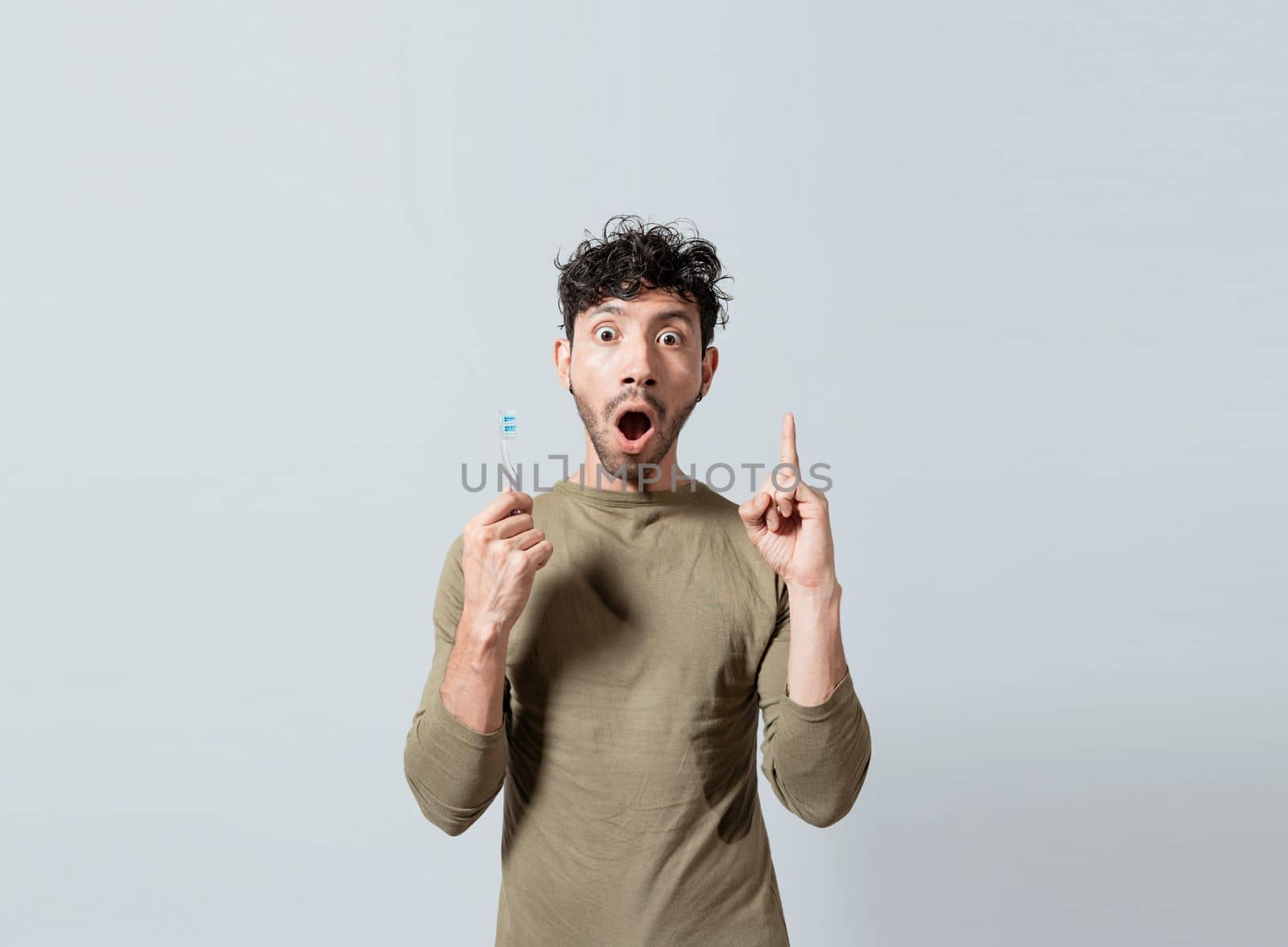 Amazed young man holding toothbrush pointing up. Guy with surprised gesture holding toothbrush pointing an advertisement. People with astonishment gesture holding toothbrush pointing a promotion