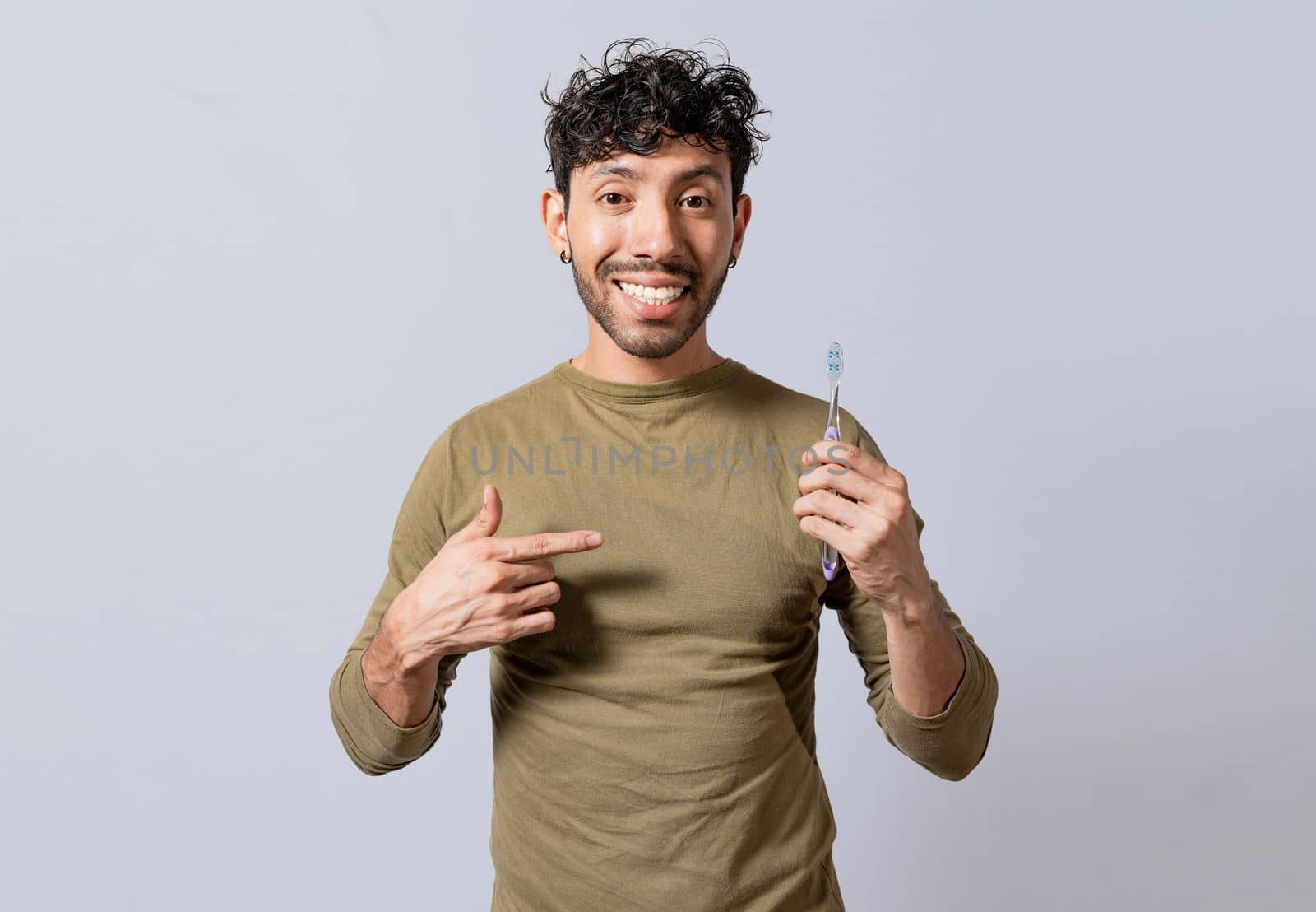 Smiling man holding and pointing at toothbrush. Handsome guy holding and pointing at toothbrush isolated. Person holding and pointing a toothbrush on isolated background
