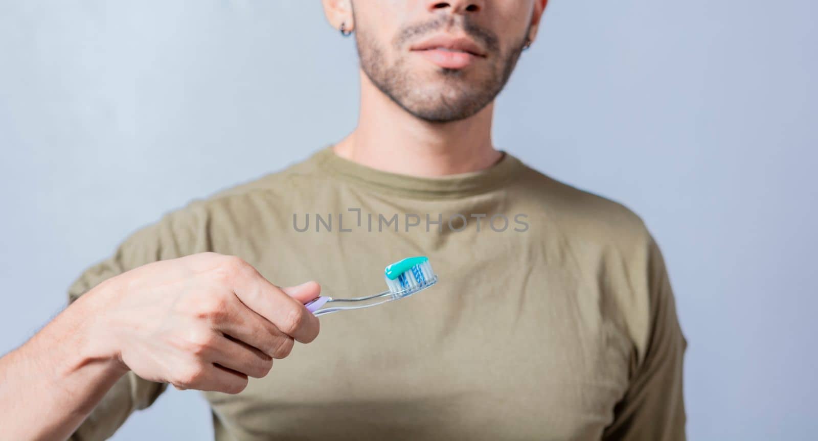 Guy with unrecognizable face holds brush with toothpaste on isolated background, shows toothbrush
